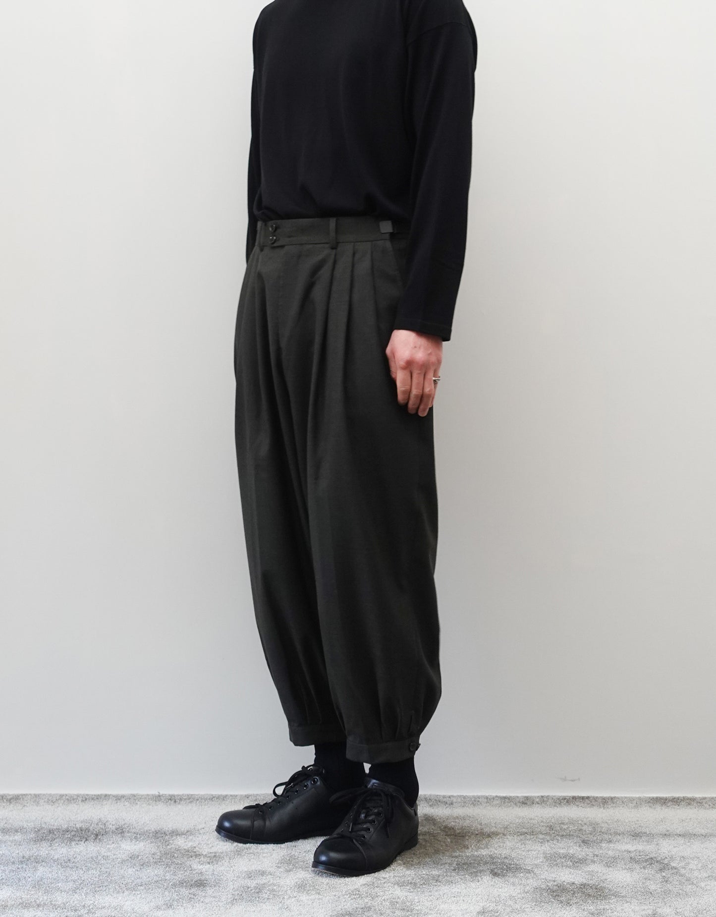VOUILLON(ヴイヨン)のTriple Tuck Harlem Slacks - DARK OLIVE(トリプルタックハーレムスラックス)。腰元の3タックによるボリューム感と、裾にかけて絞られたハーレムシルエットが特徴のダークオリーブ・ワイドパンツ。シックでモードな上品な印象。胸から下の右斜め前向きの着用画像。