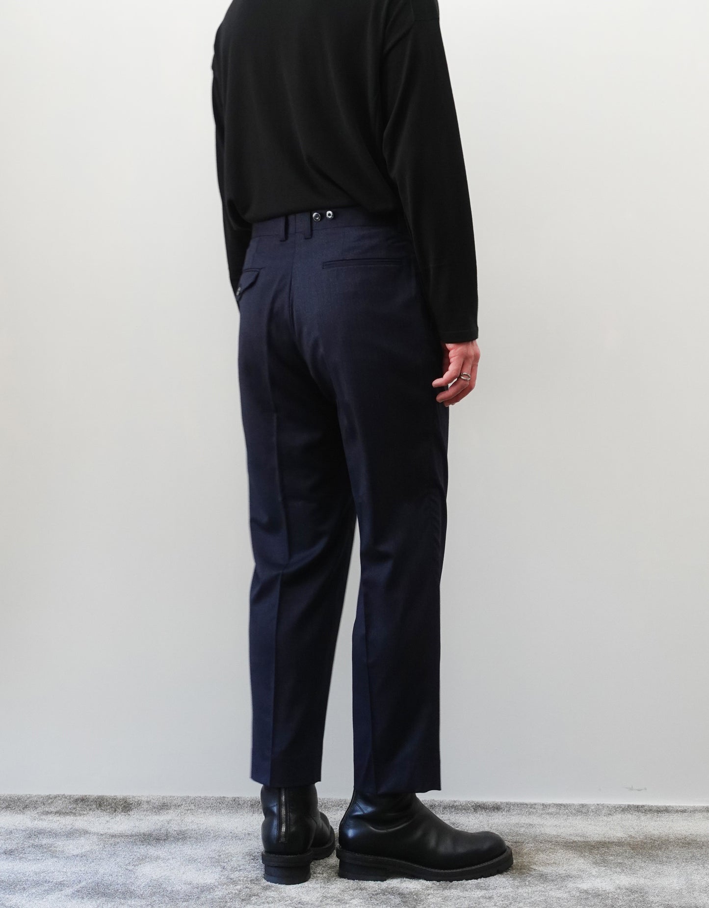 VOUILLON(ヴイヨン)のSuspender Two Tuck Trousers - Navy(サスペンダーツータックトラウザーズ)。ネイビーのツータックワイドパンツに、取り外し可能な同素材のサスペンダーを備えたディテール。サスペンダーを取り外したモデル着用背面画像。