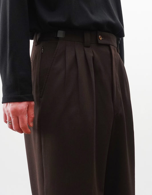 VOUILLON(ヴイヨン)のFour Pleats Wide Trousers - Dark Chocolate(4プリーツワイドトラウザーズ)。ダークチョコレート(深みのあるブラウン)のワイドシルエットと腰元の4プリーツ。モデルによる斜め左向きの着用画像のウエストアップ。