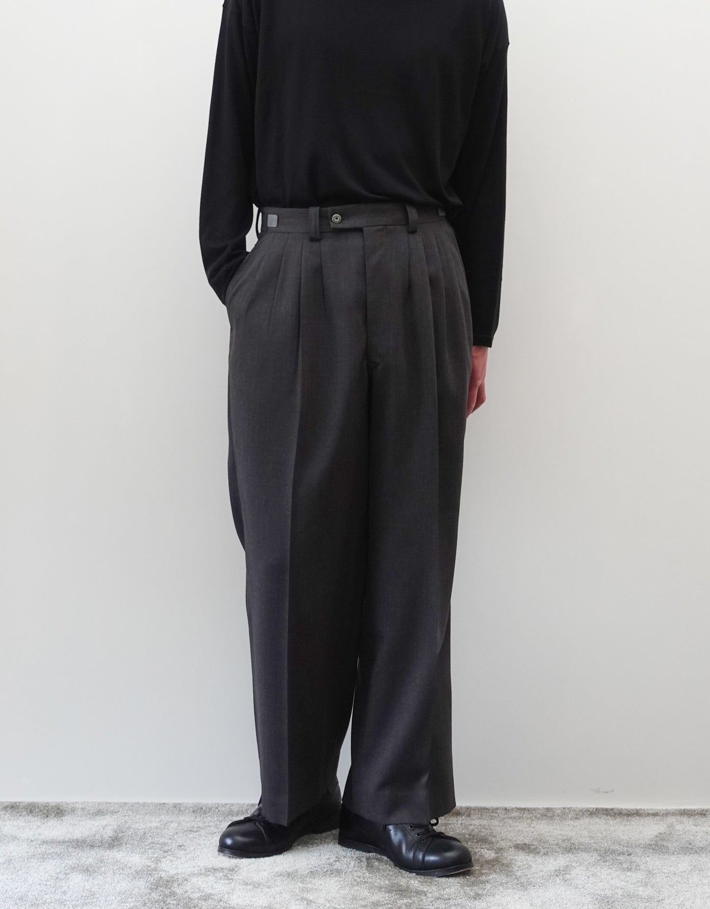 VOUILLON(ヴイヨン)のFour Pleats Wide Trousers - Gray Multi Stripe(4プリーツワイドトラウザーズ)。グレー地にマルチストライプを配した、4プリーツ仕様のワイドパンツ。ストライプによる脚長効果と立体的なシルエットが特徴。モデル着用正面(右ポケットに手を入れている)画像。