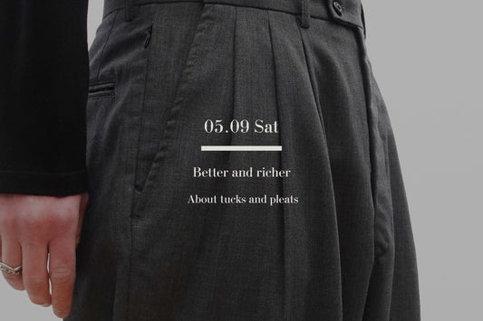 VOUILLON（ヴイヨン）マガジン「Tucks vs Pleats: Pants Styling Guide」のメインビジュアル。チャコールグレーの3タックスラックスのディテール画像に、記事タイトル「About tucks and pleats」のタイポグラフィ。