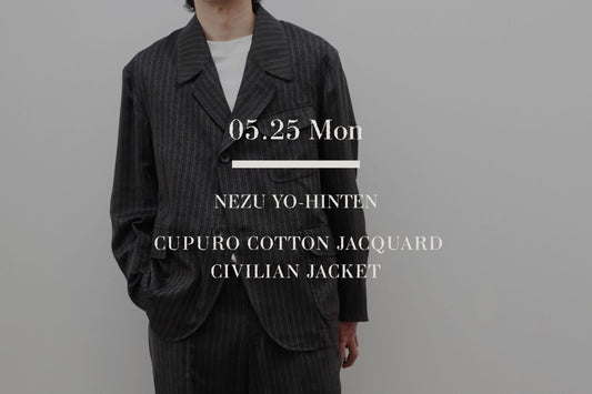 根津洋品店（NEZU YO-HINTEN）のCUPURO COTTON JACQUARD CIVILIAN JACKET（シビリアンジャケット）を着用した男性モデル（身長184cm）の全身カット。深い森を思わせるジャングルグリーンの生地に、ライトパープルの差し色が映えるペイズリー柄とピンストライプのオリジナルジャガード織。ショートパンツ（ショーツ）に長袖のジャケットを羽織り、適度な抜け感を持たせた大人のミリタリー・ショーツスタイリング。中央に白いブランドロゴテキスト。