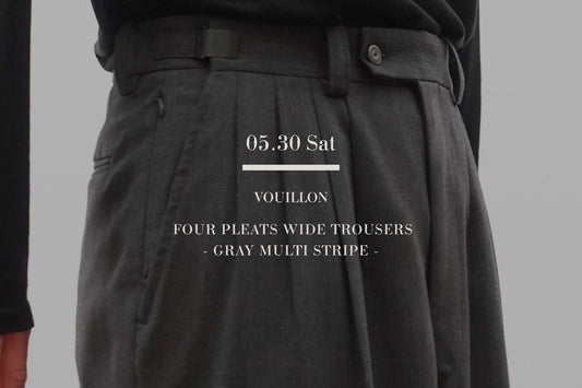 VOUILLONのFOUR PLEATS WIDE TROUSERSのGRAY MULTI STRIPEを着用した男性の腰回りクローズアップ。黒のトップスをタックインし、美しく立体的な4プリーツの折り込みと、ウエスト位置を18センチ可変できる調整アジャスターベルトの機能美を強調したミニマルなスタイリング。中央に白いブランドロゴテキスト。