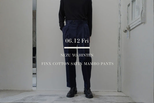 VOUILLON（ヴイヨン）マガジンのトップ画像。NEZU YO-HINTEN（根津洋品店）のフィンクスコットンサテン マンボパンツ（Mambo Pants）。上品な光沢を持つネイビーのサテン生地と、深いタックによるテーパードシルエットが特徴的なボトムスの正面全身スタイリングに、「06.12 Fri」の文字を重ねたグラフィック。