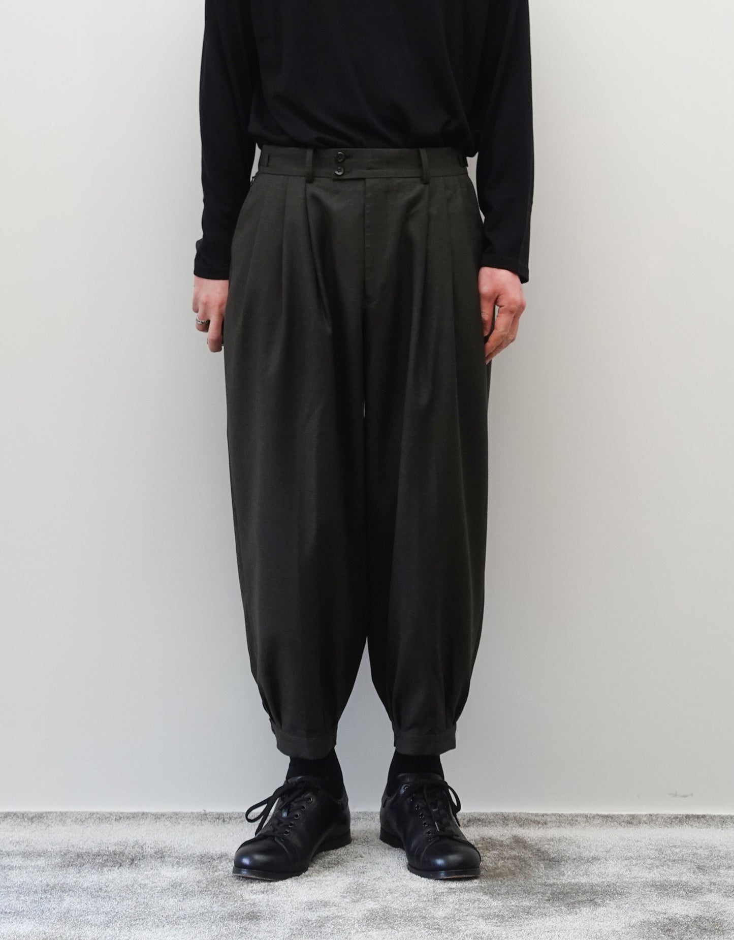 VOUILLON（ヴイヨン）のTriple Tuck Harlem Slacks - DARK OLIVE（トリプルタックハーレムスラックス）。腰元の3タックによるボリューム感と、裾にかけて絞られたハーレムシルエットが特徴のダークオリーブ・ワイドパンツ。シックでモードな上品な印象。正面の着用画像。