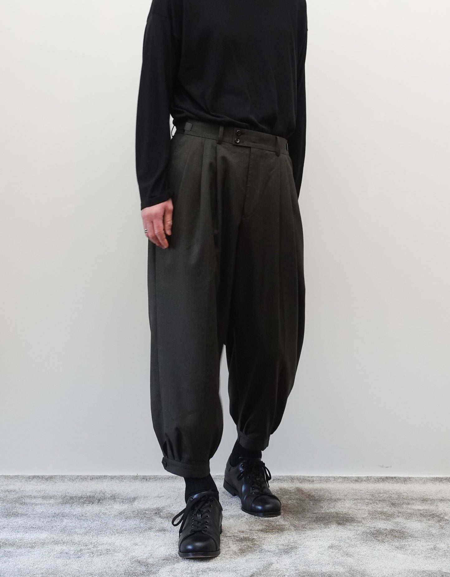 VOUILLON（ヴイヨン）のTriple Tuck Harlem Slacks - DARK OLIVE（トリプルタックハーレムスラックス）。腰元の3タックによるボリューム感と、裾にかけて絞られたハーレムシルエットが特徴のダークオリーブ・ワイドパンツ。シックでモードな上品な印象。正面の着用画像。