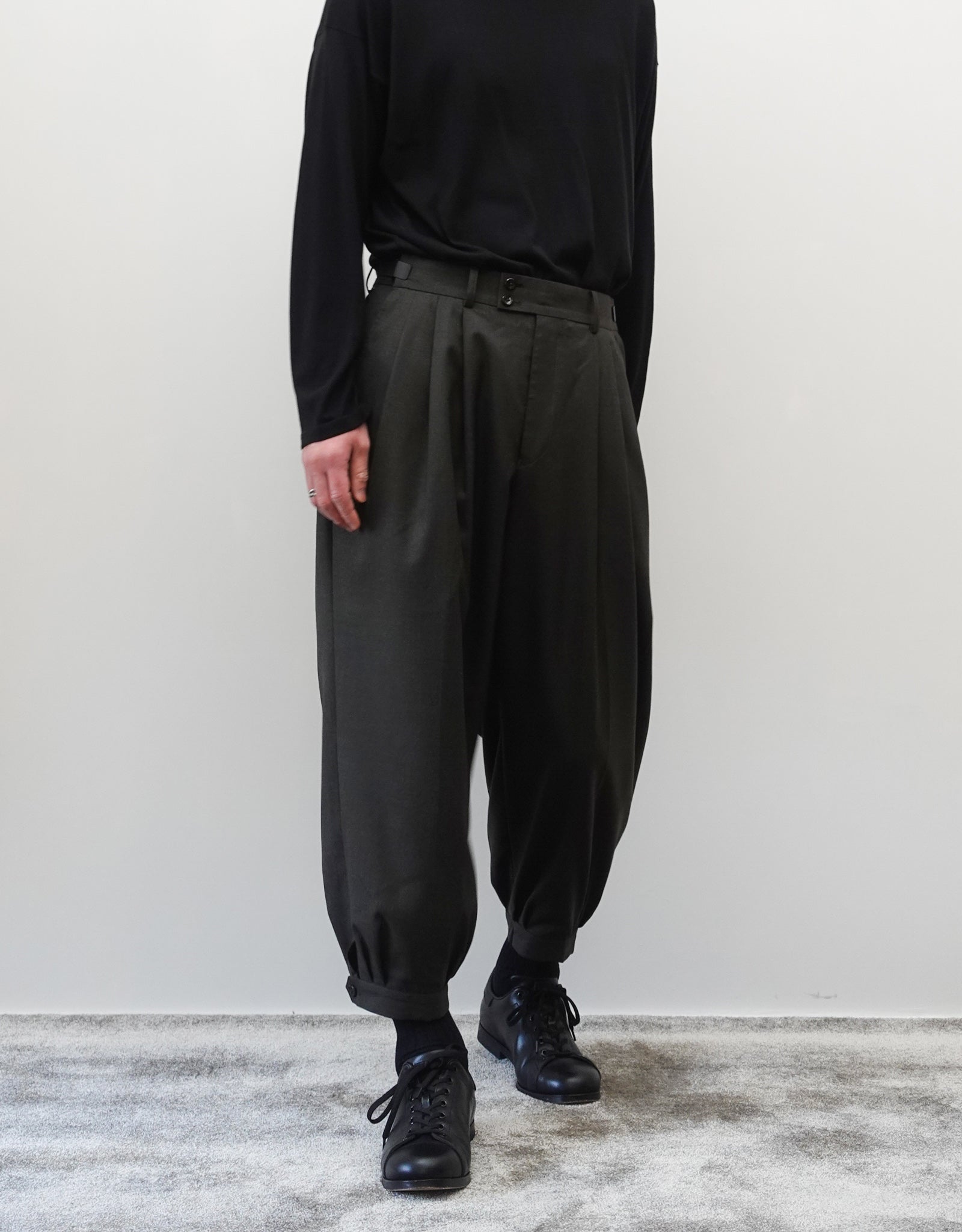 VOUILLON（ヴイヨン）のTriple Tuck Harlem Slacks - DARK OLIVE（トリプルタックハーレムスラックス）。腰元の3タックによるボリューム感と、裾にかけて絞られたハーレムシルエットが特徴のダークオリーブ・ワイドパンツ。シックでモードな上品な印象。正面の着用画像。