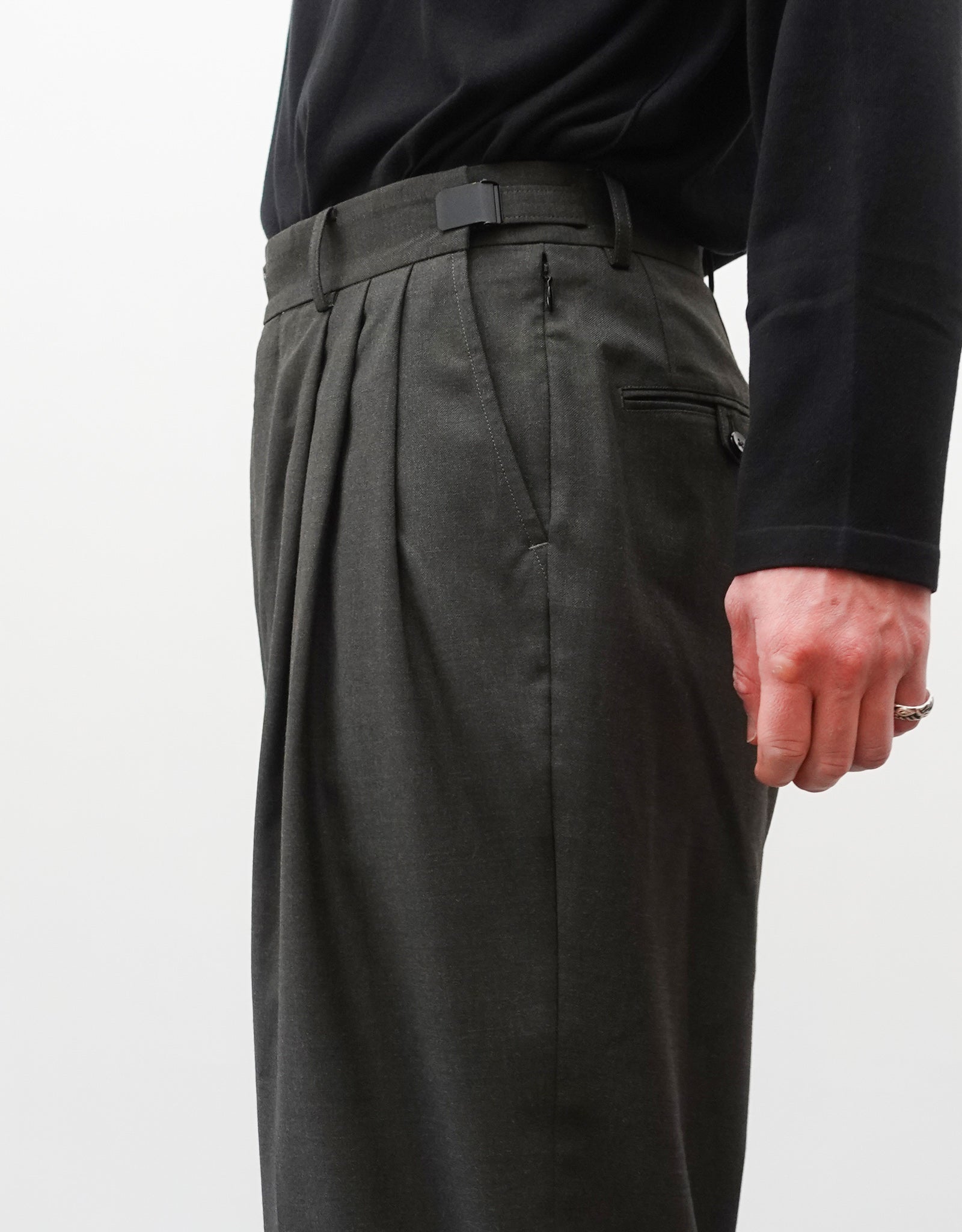 VOUILLON（ヴイヨン）のTriple Tuck Harlem Slacks - DARK OLIVE（トリプルタックハーレムスラックス）。腰元の3タックによるボリューム感と、裾にかけて絞られたハーレムシルエットが特徴のダークオリーブ・ワイドパンツ。シックでモードな上品な印象。右向き、ウエストのデザイン（スリータック、アジャスター）がわかる着用画像。