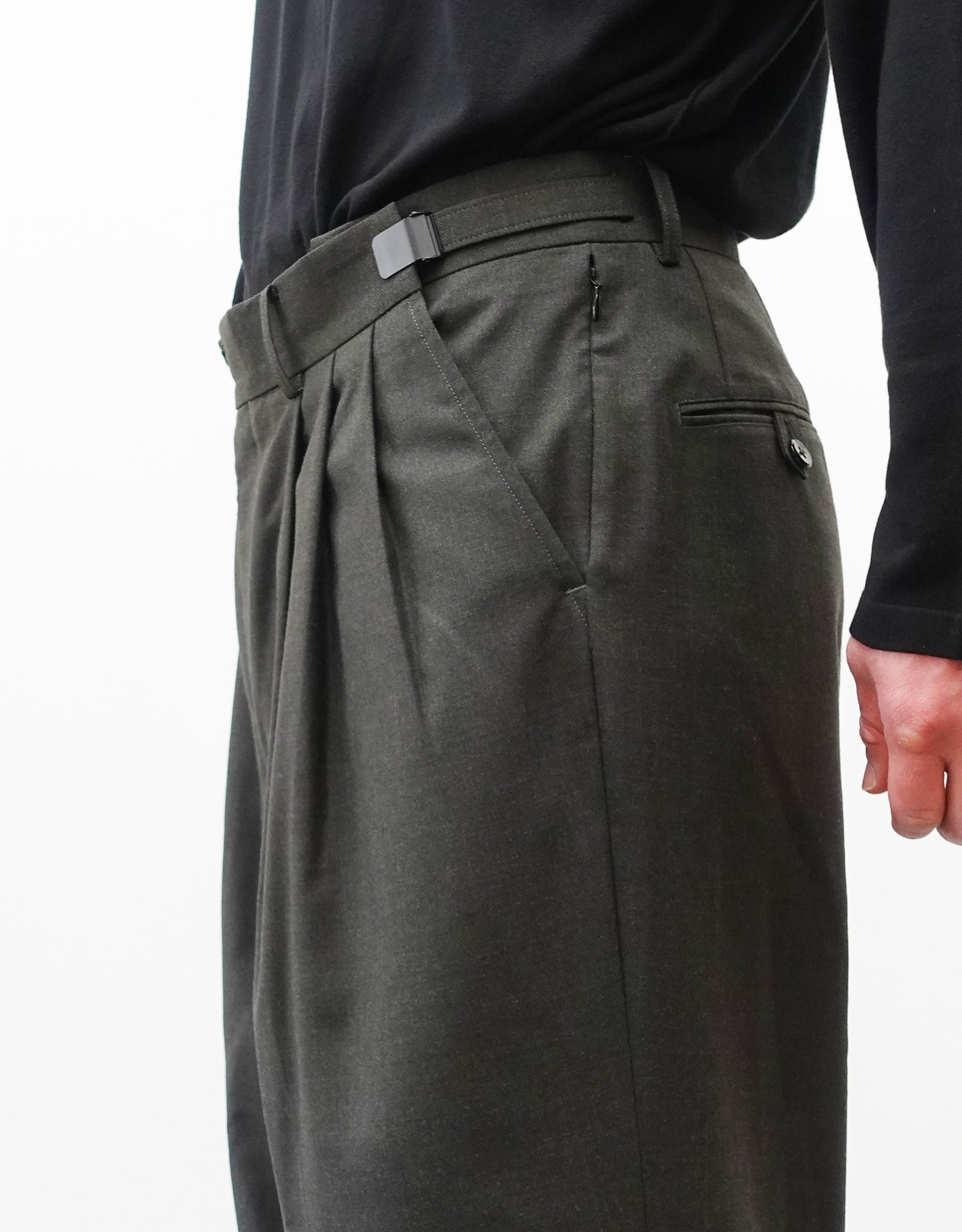 VOUILLON（ヴイヨン）のTriple Tuck Harlem Slacks - DARK OLIVE（トリプルタックハーレムスラックス）。腰元の3タックによるボリューム感と、裾にかけて絞られたハーレムシルエットが特徴のダークオリーブ・ワイドパンツ。シックでモードな上品な印象。右向き、ウエストのデザイン（スリータック、アジャスターを最大限開く）がわかる着用画像。