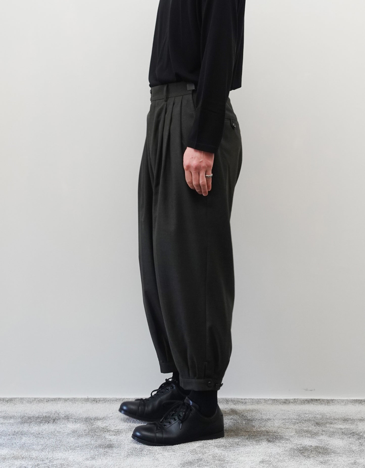 VOUILLON（ヴイヨン）のTriple Tuck Harlem Slacks - DARK OLIVE（トリプルタックハーレムスラックス）。腰元の3タックによるボリューム感と、裾にかけて絞られたハーレムシルエットが特徴のダークオリーブ・ワイドパンツ。シックでモードな上品な印象。胸から下の右向きの着用画像。