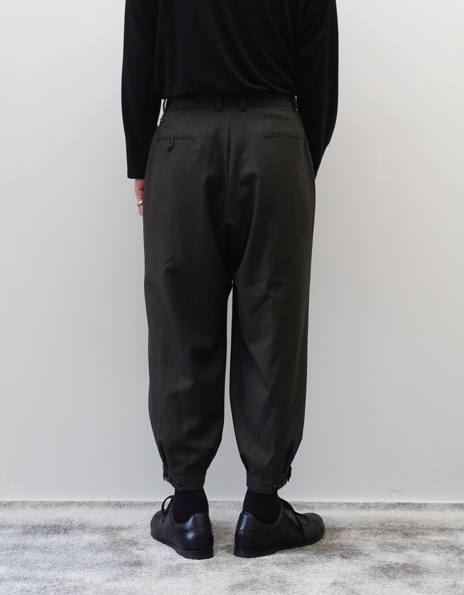 VOUILLON（ヴイヨン）のTriple Tuck Harlem Slacks - DARK OLIVE（トリプルタックハーレムスラックス）。腰元の3タックによるボリューム感と、裾にかけて絞られたハーレムシルエットが特徴のダークオリーブ・ワイドパンツ。シックでモードな上品な印象。胸から下の背面の着用画像。