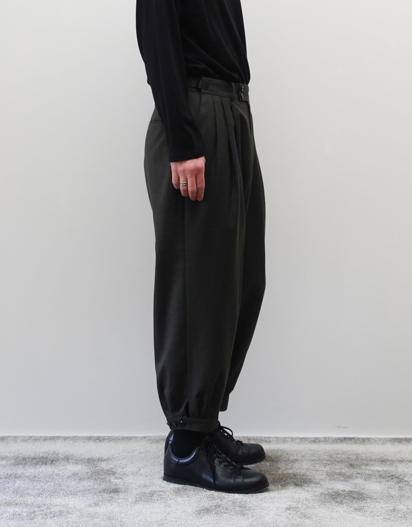 VOUILLON（ヴイヨン）のTriple Tuck Harlem Slacks - DARK OLIVE（トリプルタックハーレムスラックス）。腰元の3タックによるボリューム感と、裾にかけて絞られたハーレムシルエットが特徴のダークオリーブ・ワイドパンツ。シックでモードな上品な印象。胸から下の左向きの着用画像。