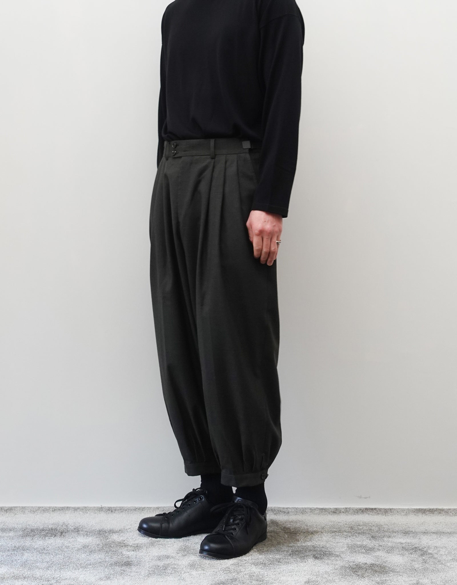 VOUILLON（ヴイヨン）のTriple Tuck Harlem Slacks - DARK OLIVE（トリプルタックハーレムスラックス）。腰元の3タックによるボリューム感と、裾にかけて絞られたハーレムシルエットが特徴のダークオリーブ・ワイドパンツ。シックでモードな上品な印象。胸から下の右斜め前向きの着用画像。