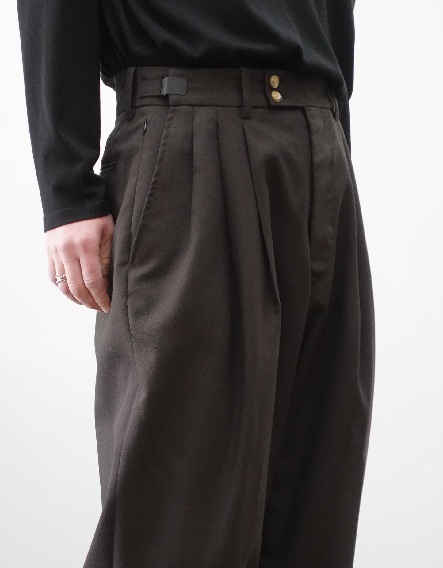 VOUILLON（ヴイヨン）のTriple Tuck Harlem Slacks - DARK BROWN（トリプルタックハーレムスラックス）。腰元の3タックによるボリューム感と、裾にかけて絞られたハーレムシルエットが特徴のブラック・ワイドパンツ。色味とウエストのデザインがわかる寄り画像。