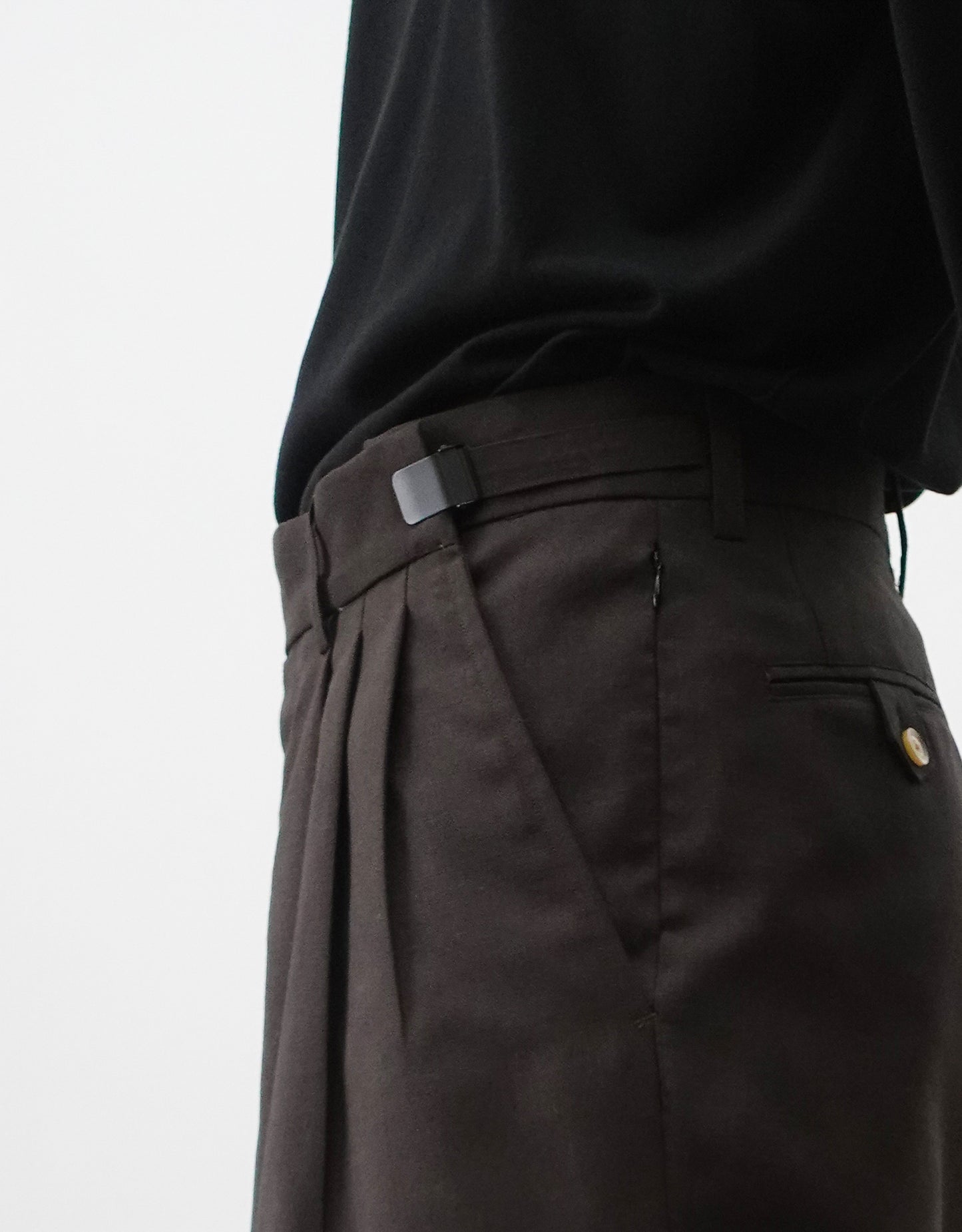 VOUILLON（ヴイヨン）のTriple Tuck Harlem Slacks - DARK BROWN（トリプルタックハーレムスラックス）。腰元の3タックによるボリューム感と、裾にかけて絞られたハーレムシルエットが特徴のブラック・ワイドパンツ。色味とウエストのアジャスター開閉の状態がわかる寄り画像。