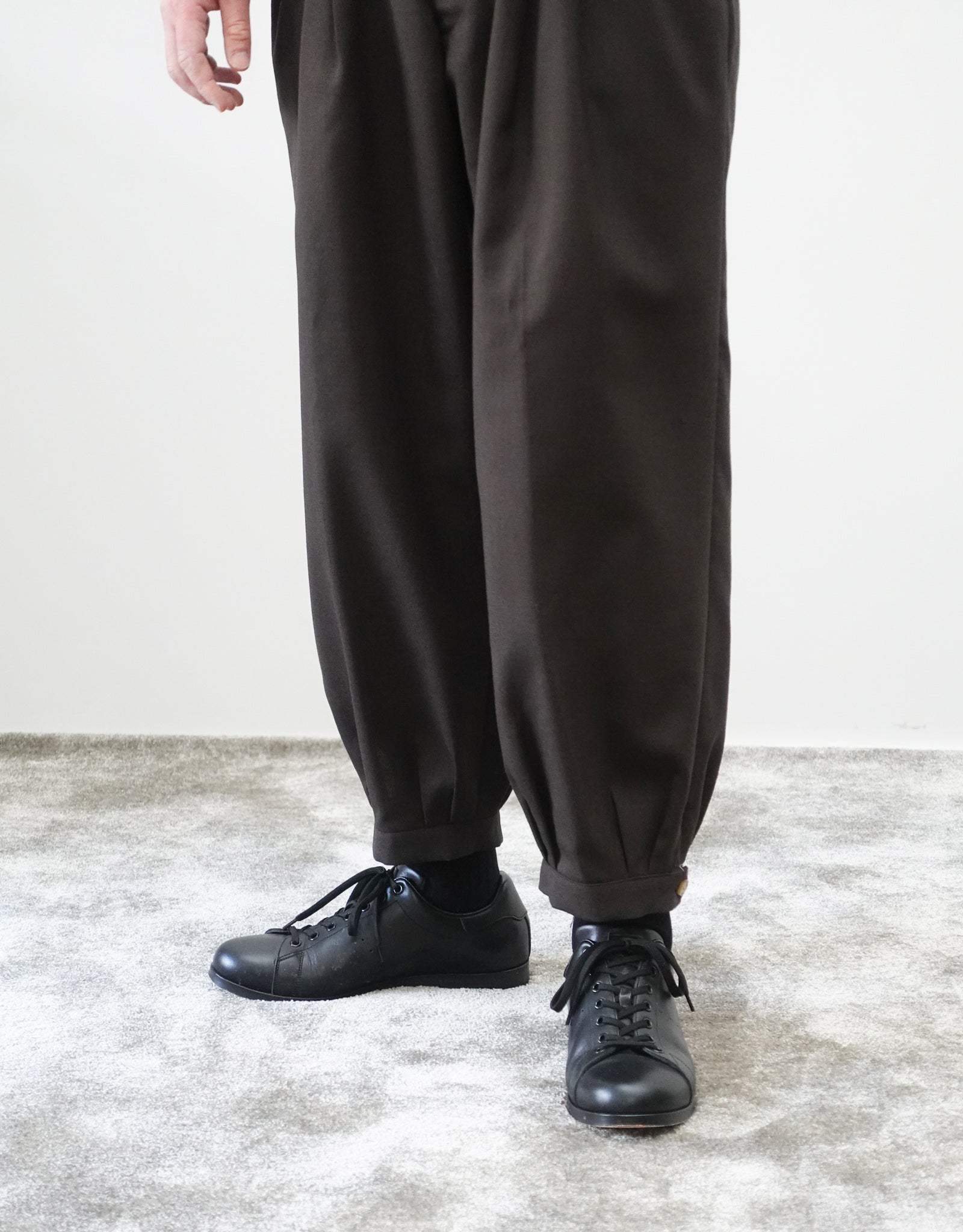VOUILLON（ヴイヨン）のTriple Tuck Harlem Slacks - DARK BROWN（トリプルタックハーレムスラックス）。腰元の3タックによるボリューム感と、裾にかけて絞られたハーレムシルエットが特徴のブラック・ワイドパンツ。裾のエイトタックがわかる寄り画像。