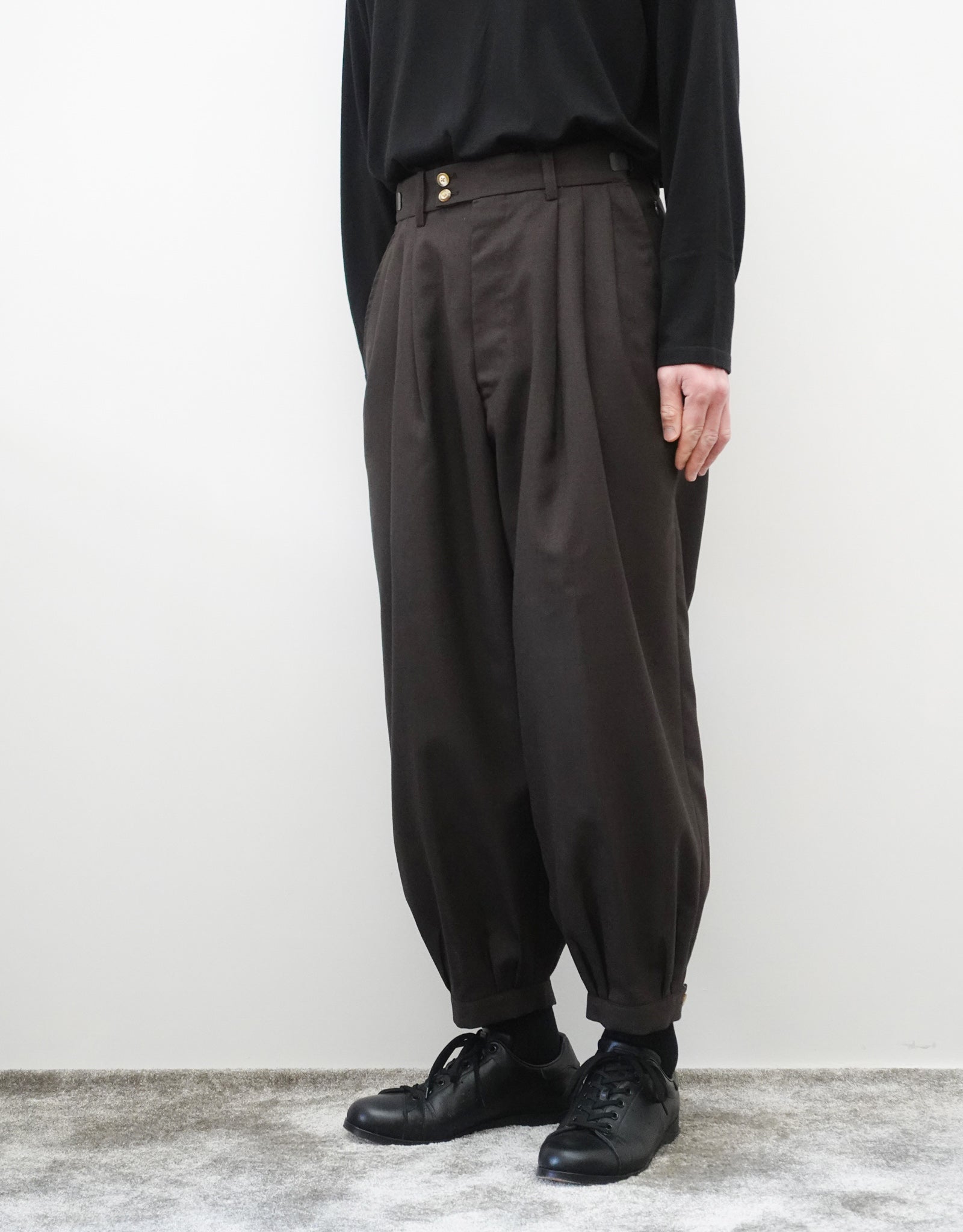 VOUILLON（ヴイヨン）のTriple Tuck Harlem Slacks - DARK BROWN（トリプルタックハーレムスラックス）。腰元の3タックによるボリューム感と、裾にかけて絞られたハーレムシルエットが特徴のブラック・ワイドパンツ。色味とシルエットがわかる着用右斜め前画像。