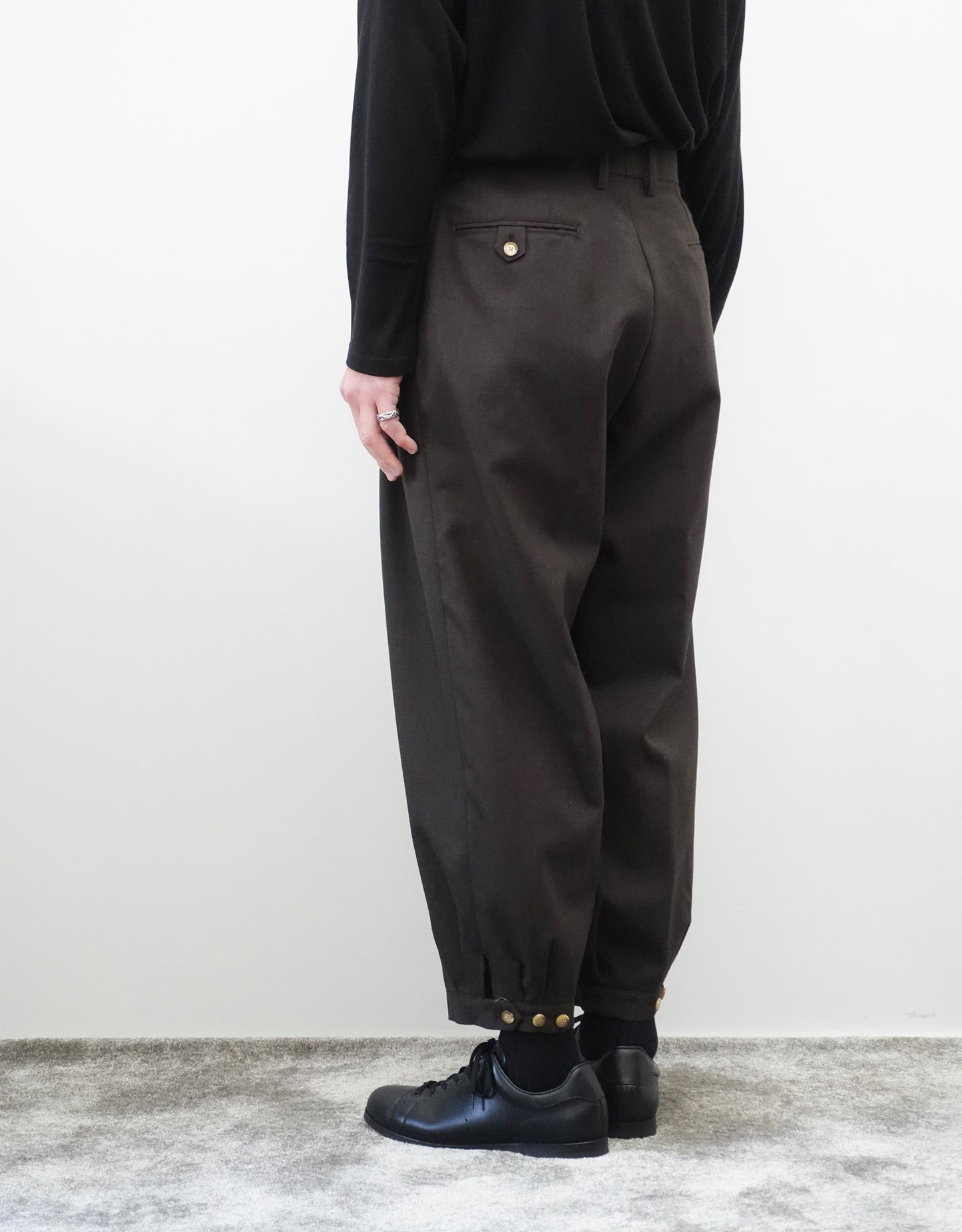 VOUILLON（ヴイヨン）のTriple Tuck Harlem Slacks - DARK BROWN（トリプルタックハーレムスラックス）。腰元の3タックによるボリューム感と、裾にかけて絞られたハーレムシルエットが特徴のブラック・ワイドパンツ。色味とシルエットがわかる着用背面画像。