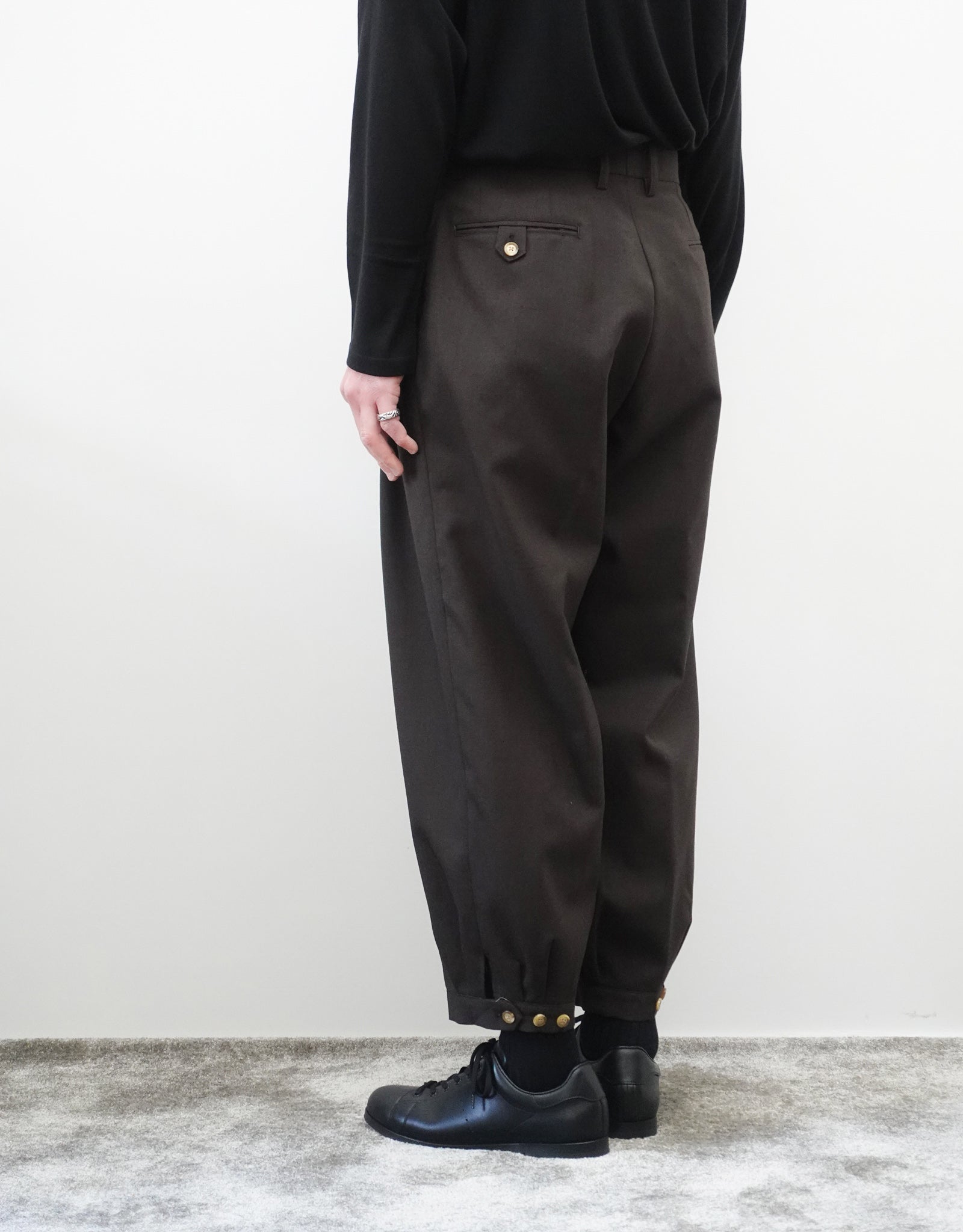 VOUILLON（ヴイヨン）のTriple Tuck Harlem Slacks - DARK BROWN（トリプルタックハーレムスラックス）。腰元の3タックによるボリューム感と、裾にかけて絞られたハーレムシルエットが特徴のブラック・ワイドパンツ。色味とシルエットがわかる着用背面画像。