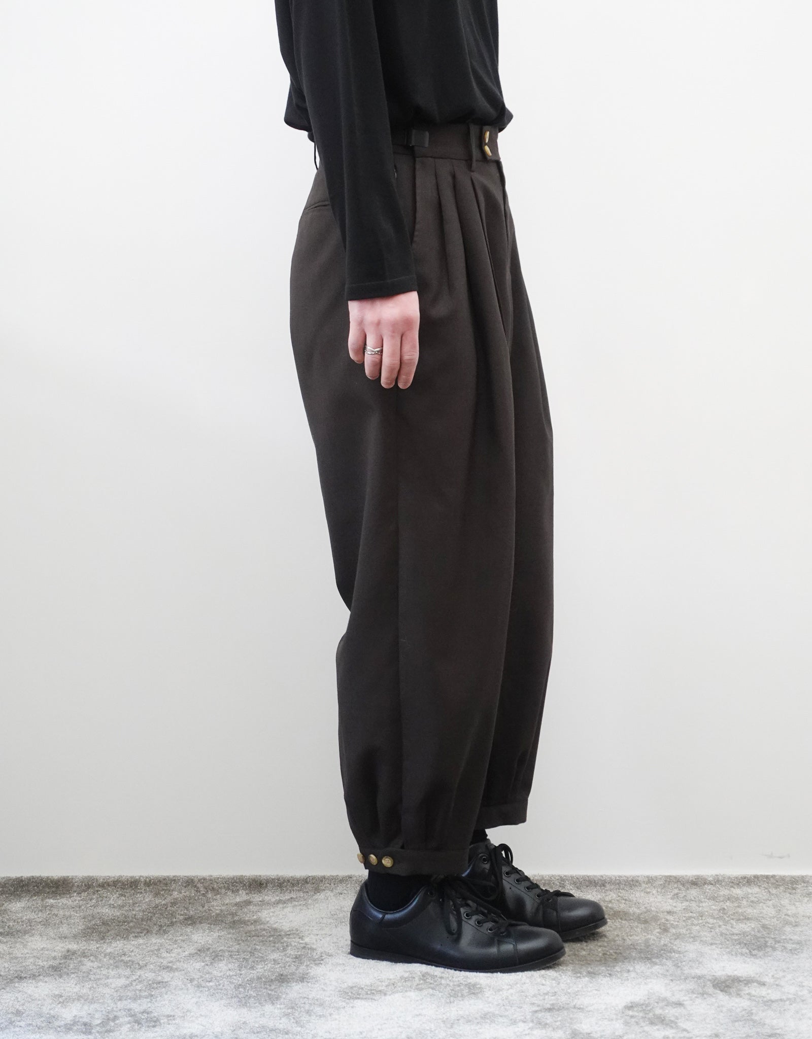 VOUILLON（ヴイヨン）のTriple Tuck Harlem Slacks - DARK BROWN（トリプルタックハーレムスラックス）。腰元の3タックによるボリューム感と、裾にかけて絞られたハーレムシルエットが特徴のブラック・ワイドパンツ。色味とシルエットがわかる着用左向き画像。