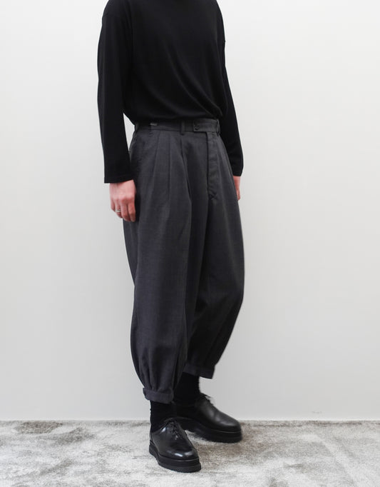 VOUILLON（ヴイヨン）のTriple Tuck Harlem Slacks - DARK GRAY（トリプルタックハーレムスラックス）。腰元の3タックによるボリューム感と、裾にかけて絞られたハーレムシルエットが特徴のダークグレー・ワイドパンツ。左斜め前を向いた着用画像。