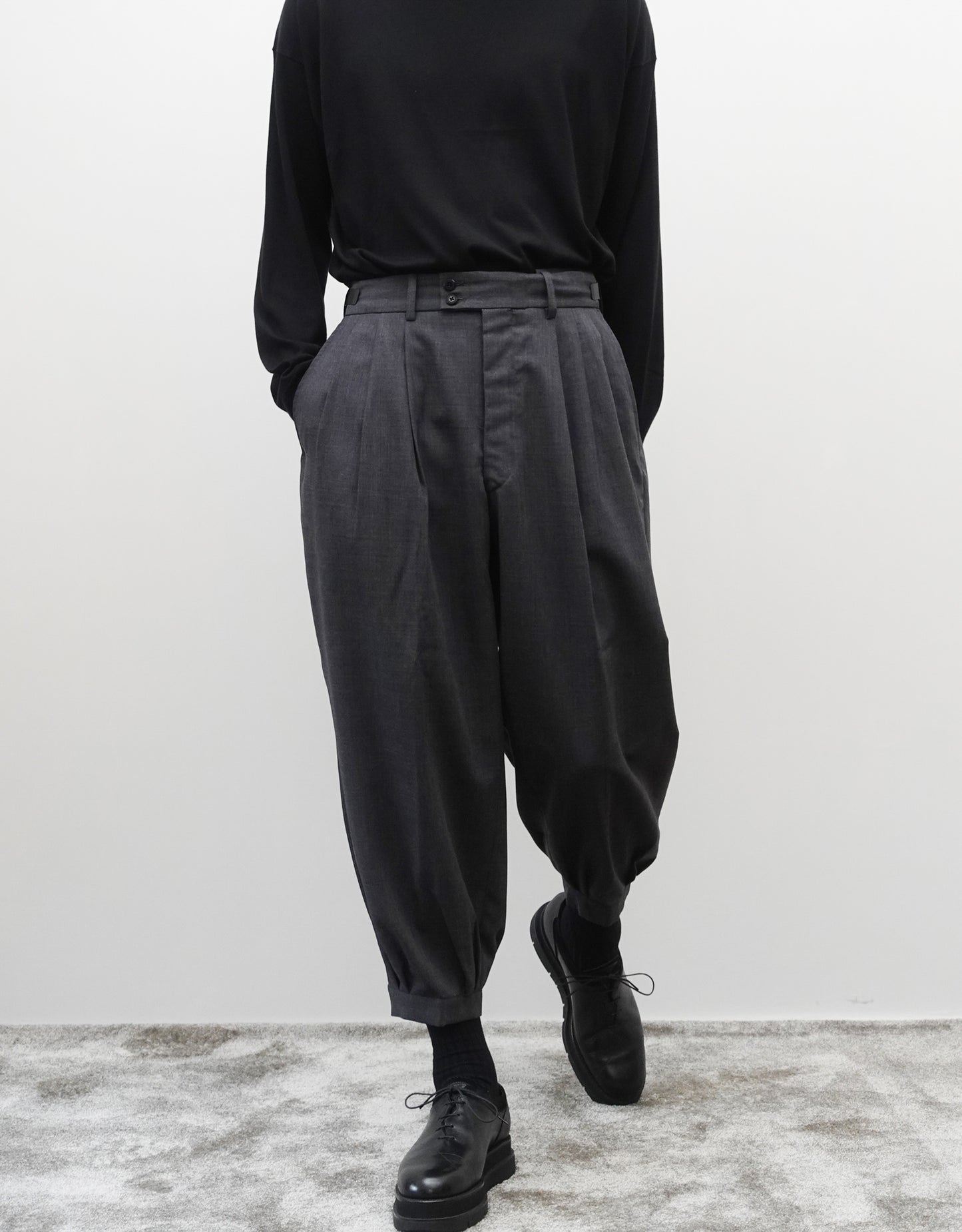 VOUILLON（ヴイヨン）のTriple Tuck Harlem Slacks - DARK GRAY（トリプルタックハーレムスラックス）。腰元の3タックによるボリューム感と、裾にかけて絞られたハーレムシルエットが特徴のダークグレー・ワイドパンツ。正面（ポケットに手を入れている）の着用画像。