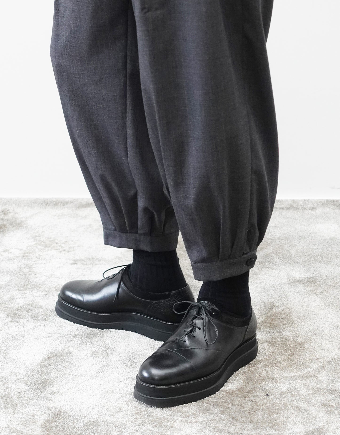 VOUILLON（ヴイヨン）のTriple Tuck Harlem Slacks - DARK GRAY（トリプルタックハーレムスラックス）。腰元の3タックによるボリューム感と、裾にかけて絞られたハーレムシルエットが特徴のダークグレー・ワイドパンツ。裾のエイトタック（ディティール）の着用画像。