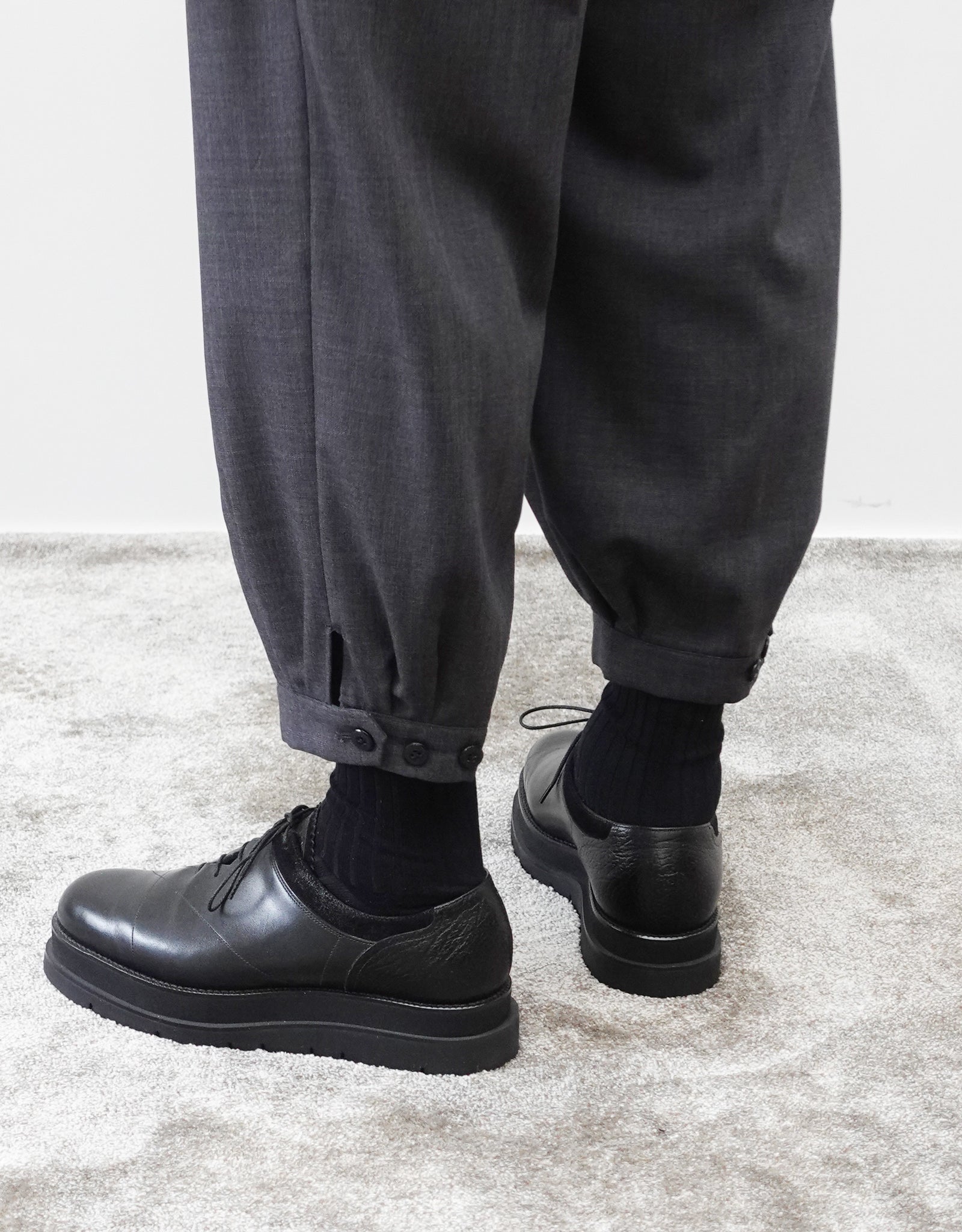 VOUILLON（ヴイヨン）のTriple Tuck Harlem Slacks - DARK GRAY（トリプルタックハーレムスラックス）。腰元の3タックによるボリューム感と、裾にかけて絞られたハーレムシルエットが特徴のダークグレー・ワイドパンツ。裾のエイトタック（ディティール）とシルエット変更できる３つボタンの着用画像。