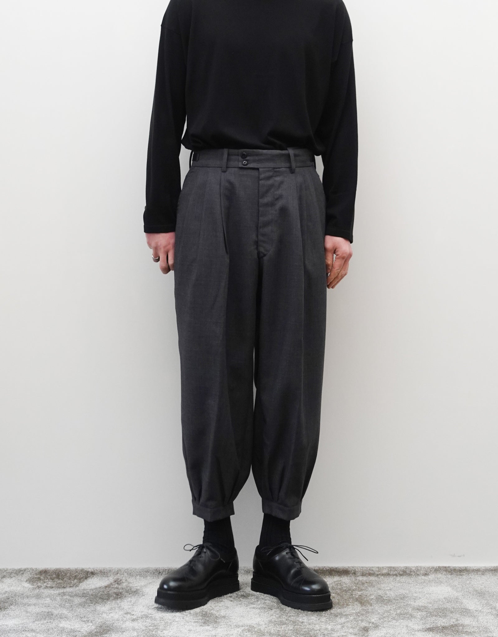 VOUILLON（ヴイヨン）のTriple Tuck Harlem Slacks - DARK GRAY（トリプルタックハーレムスラックス）。腰元の3タックによるボリューム感と、裾にかけて絞られたハーレムシルエットが特徴のダークグレー・ワイドパンツ。正面の着用画像。