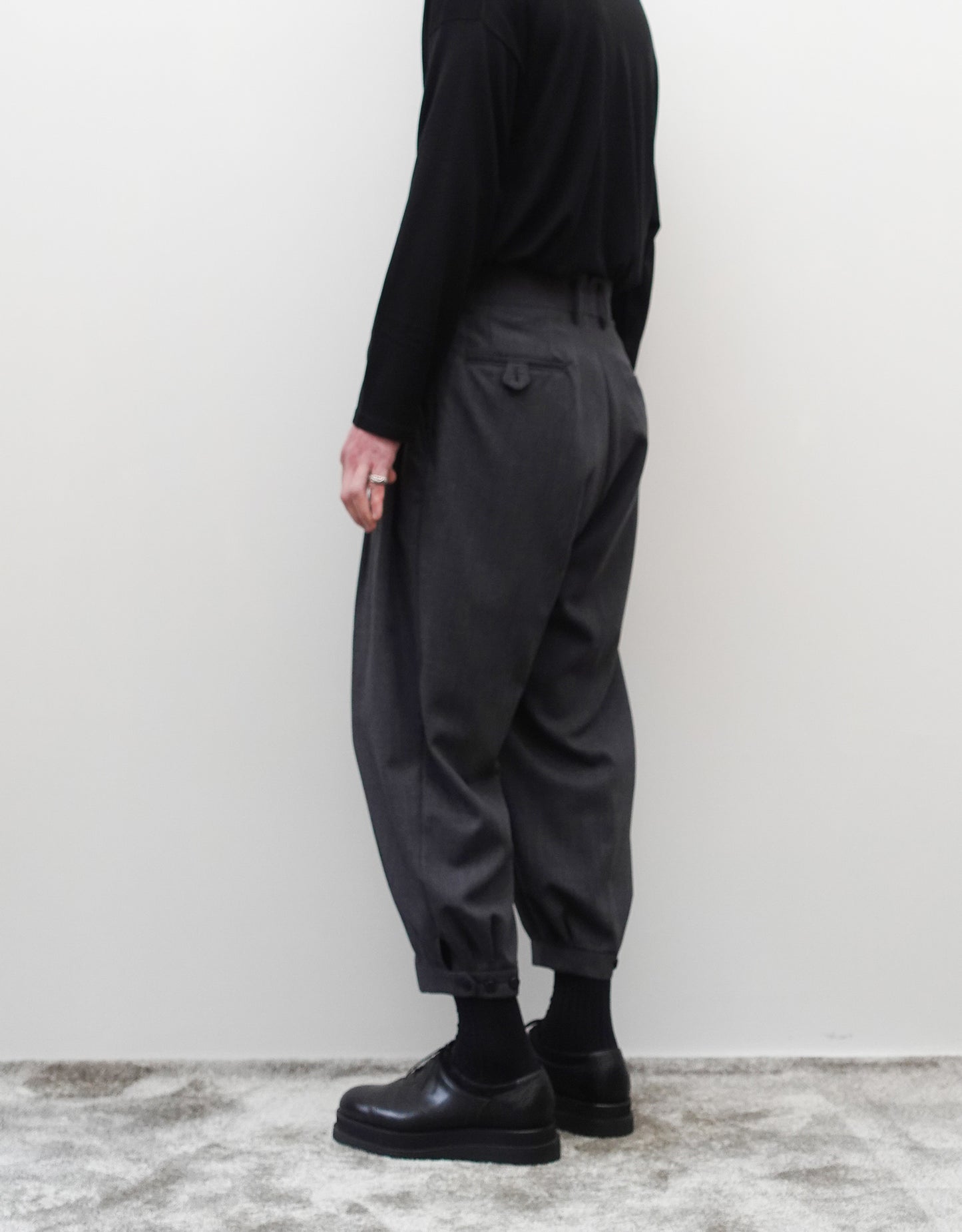 VOUILLON（ヴイヨン）のTriple Tuck Harlem Slacks - DARK GRAY（トリプルタックハーレムスラックス）。腰元の3タックによるボリューム感と、裾にかけて絞られたハーレムシルエットが特徴のダークグレー・ワイドパンツ。右横向きの着用画像。