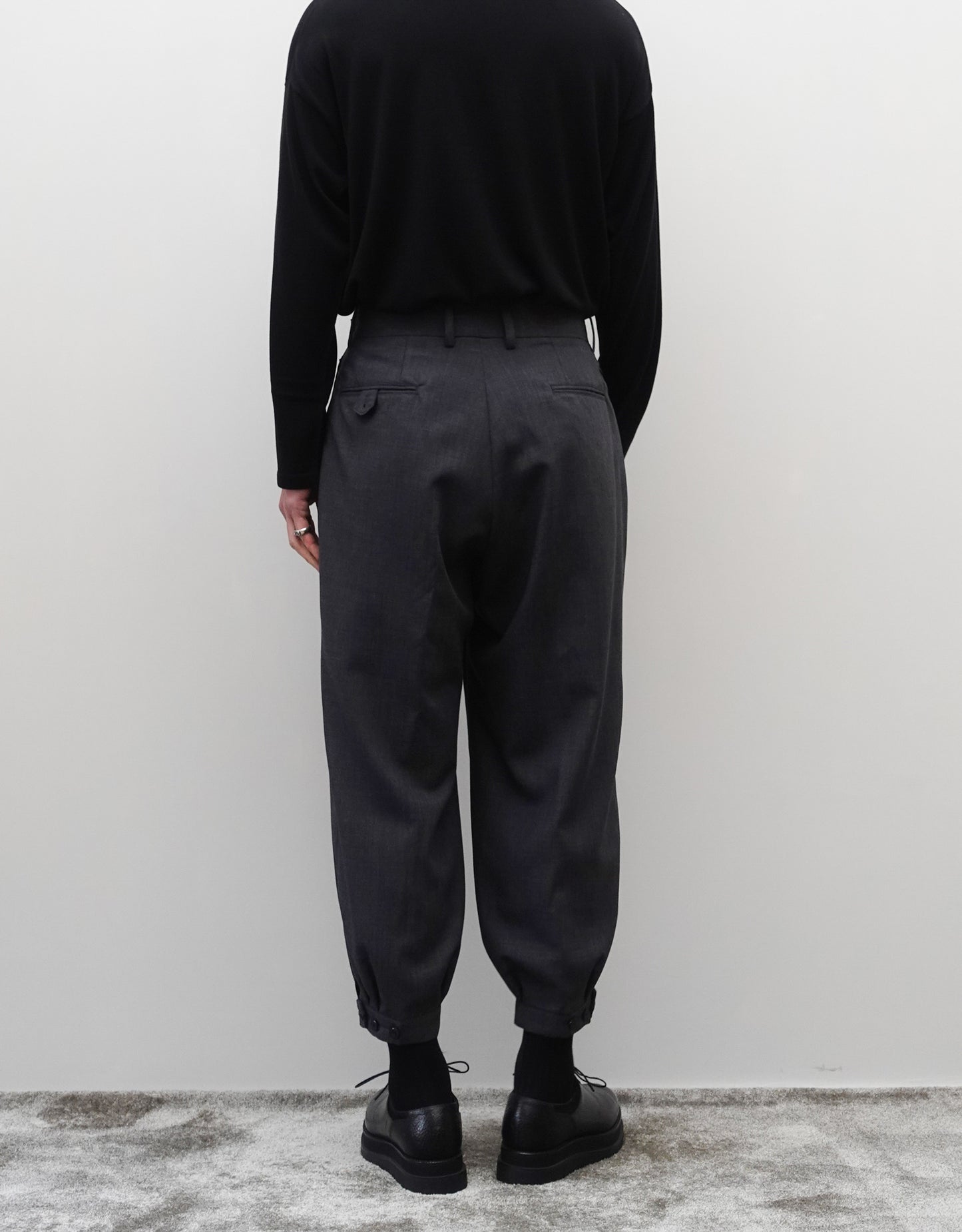 VOUILLON（ヴイヨン）のTriple Tuck Harlem Slacks - DARK GRAY（トリプルタックハーレムスラックス）。腰元の3タックによるボリューム感と、裾にかけて絞られたハーレムシルエットが特徴のダークグレー・ワイドパンツ。背面の着用画像。