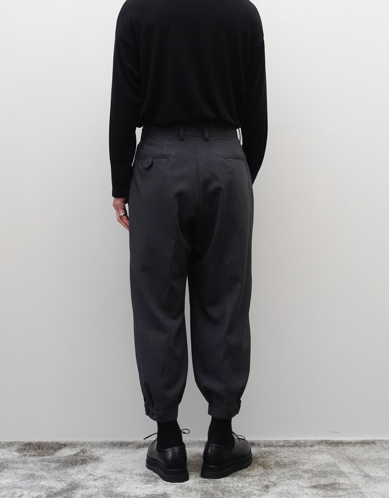 VOUILLON（ヴイヨン）のTriple Tuck Harlem Slacks - DARK GRAY（トリプルタックハーレムスラックス）。腰元の3タックによるボリューム感と、裾にかけて絞られたハーレムシルエットが特徴のダークグレー・ワイドパンツ。背面の着用画像。