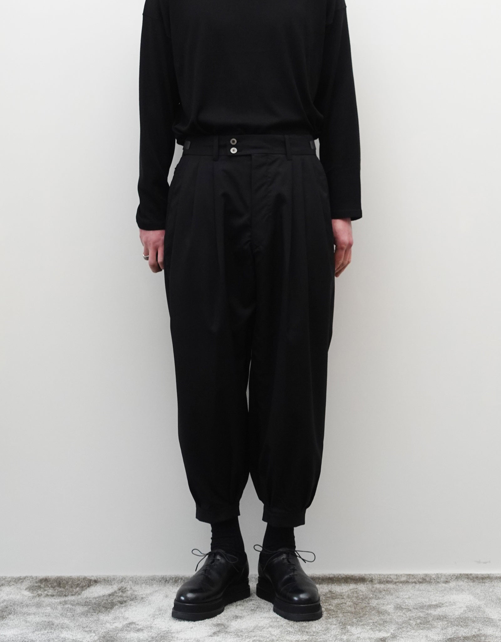 VOUILLON（ヴイヨン）のTriple Tuck Harlem Slacks - Black（トリプルタックハーレムスラックス）。腰元の3タックによるボリューム感と、裾にかけて絞られたハーレムシルエットが特徴のブラック・ワイドパンツ。モードなオールブラックのスタイリング。