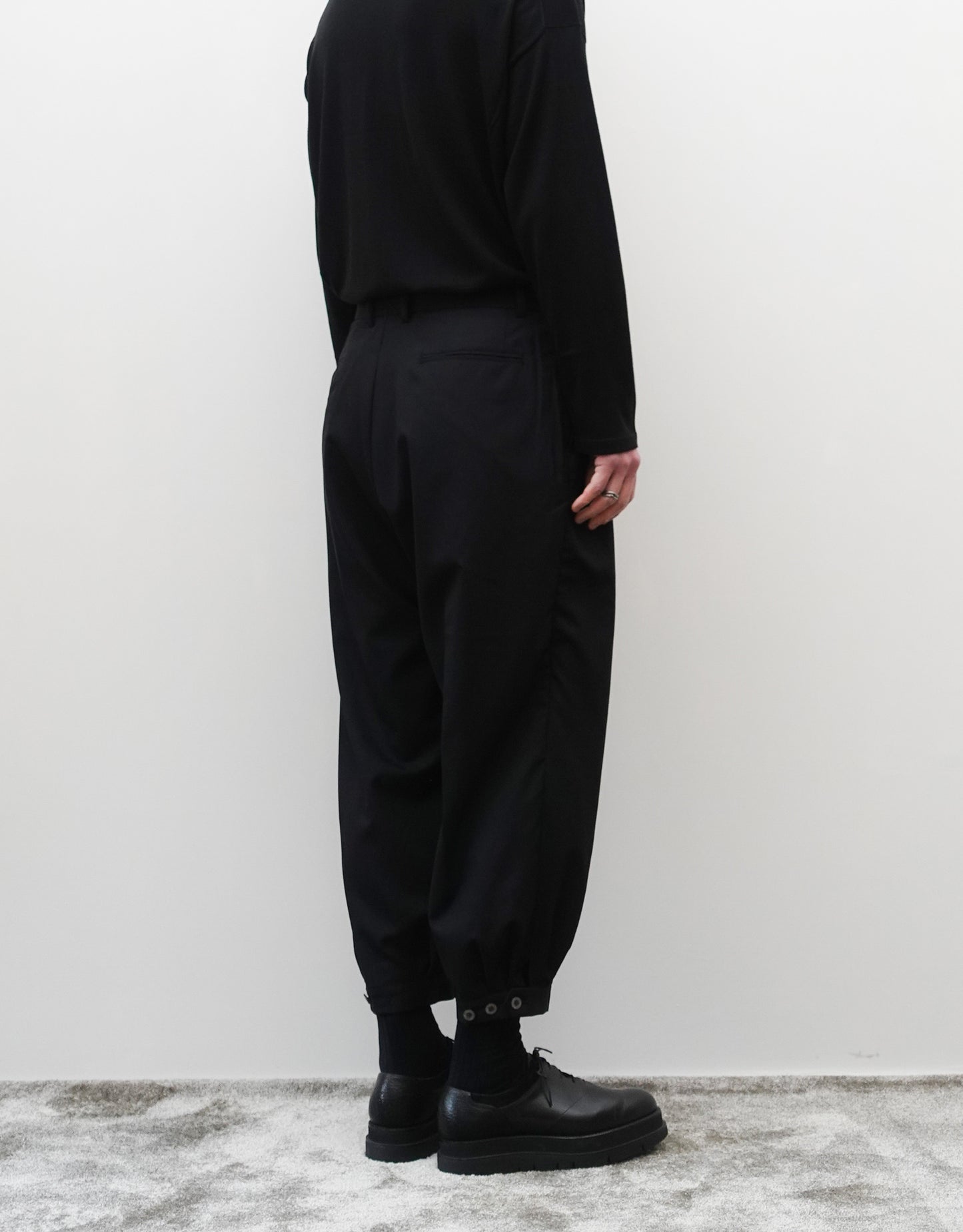 VOUILLON（ヴイヨン）のTriple Tuck Harlem Slacks - Black（トリプルタックハーレムスラックス）。腰元の3タックによるボリューム感と、裾にかけて絞られたハーレムシルエットが特徴のブラック・コクーンシルエットのパンツ。シルエットがわかる背面の着用画像。