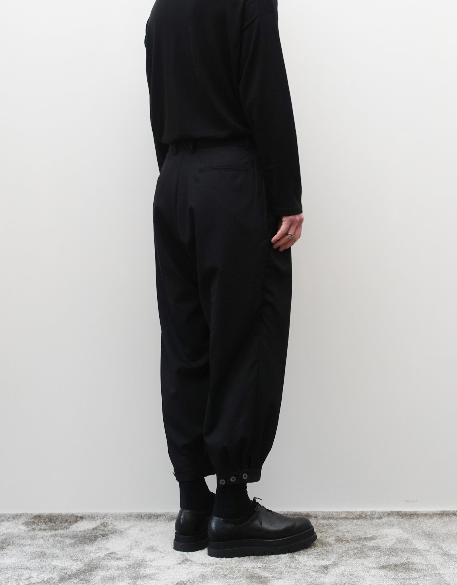 VOUILLON（ヴイヨン）のTriple Tuck Harlem Slacks - Black（トリプルタックハーレムスラックス）。腰元の3タックによるボリューム感と、裾にかけて絞られたハーレムシルエットが特徴のブラック・コクーンシルエットのパンツ。シルエットがわかる背面の着用画像。