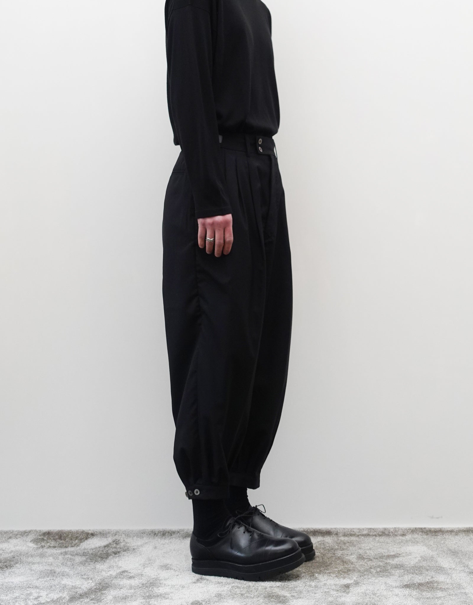 VOUILLON（ヴイヨン）のTriple Tuck Harlem Slacks - Black（トリプルタックハーレムスラックス）。腰元の3タックによるボリューム感と、裾にかけて絞られたハーレムシルエットが特徴のブラック・コクーンシルエットのパンツ。シルエットがわかる左向きの着用画像。