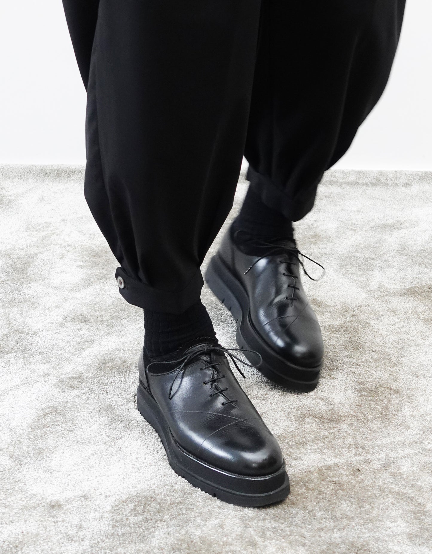 VOUILLON（ヴイヨン）のTriple Tuck Harlem Slacks - Black（トリプルタックハーレムスラックス）。腰元の3タックによるボリューム感と、裾にかけて絞られたハーレムシルエットが特徴のブラック・コクーンシルエットのパンツ。裾のエイトタックをアップにした正面から撮影。