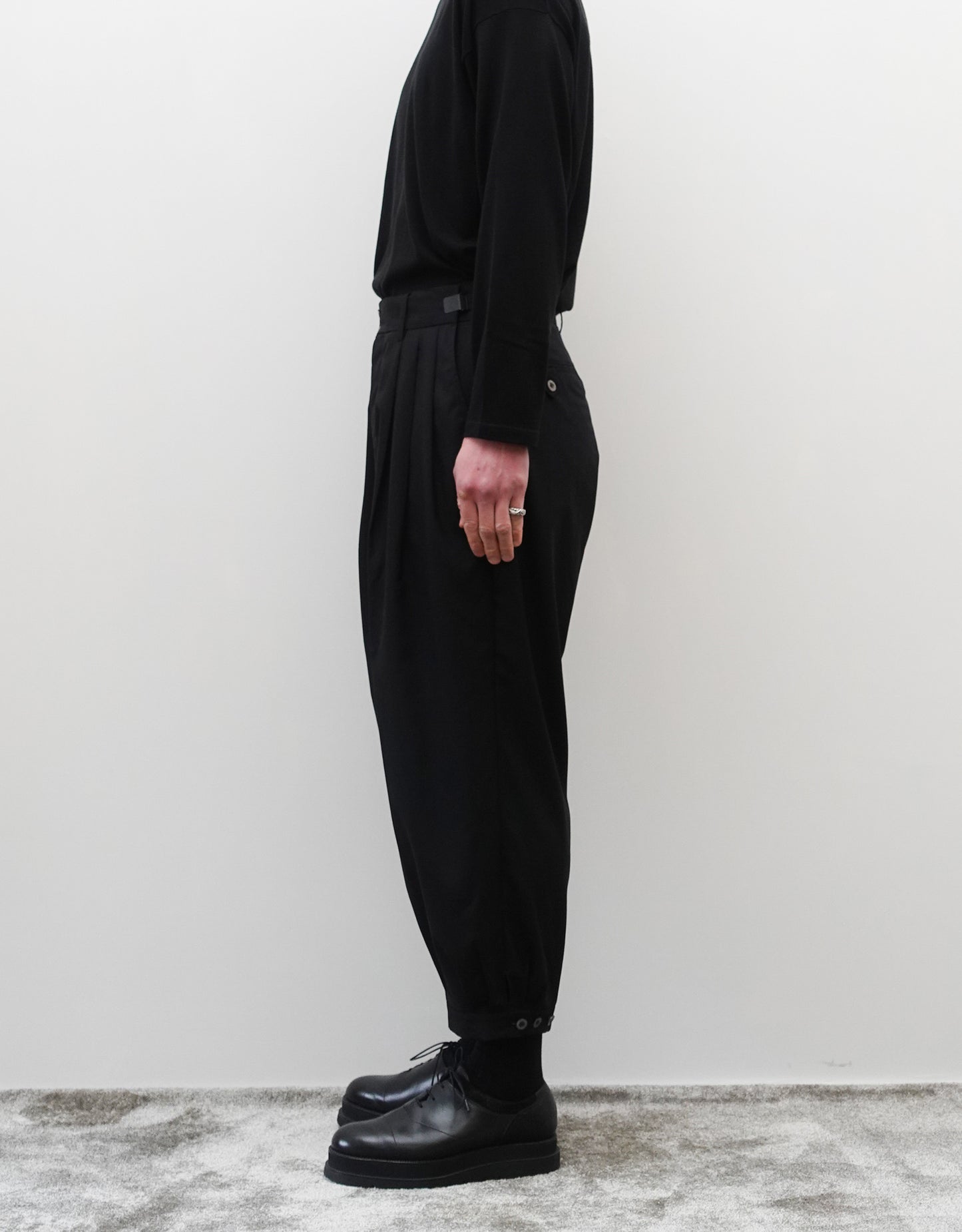 VOUILLON（ヴイヨン）のTriple Tuck Harlem Slacks - Black（トリプルタックハーレムスラックス）。腰元の3タックによるボリューム感と、裾にかけて絞られたハーレムシルエットが特徴のブラック・コクーンシルエットのパンツ。シルエットがわかる右向き画像。