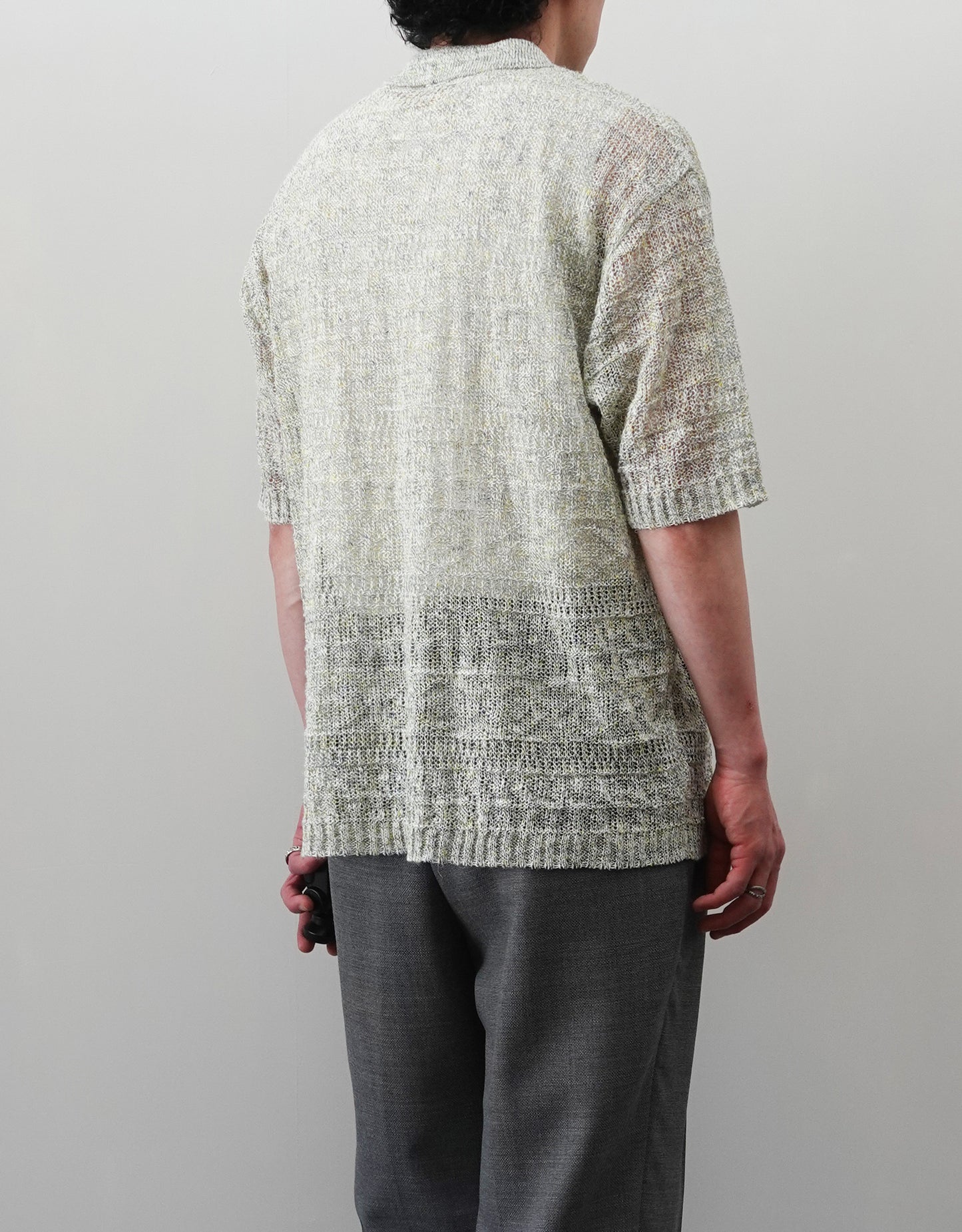 VOUILLON（ヴイヨン）のOpenwork Stitch Polo Linen Knit Shirt（オープンワークステッチポロリネンニットシャツ）。涼しげな透かし編み（オープンワーク）を施した、リネン素材のポロ襟ニットシャツ。独特の透け感とリラクシングなシルエットが特徴。モデル着用左後向き画像。