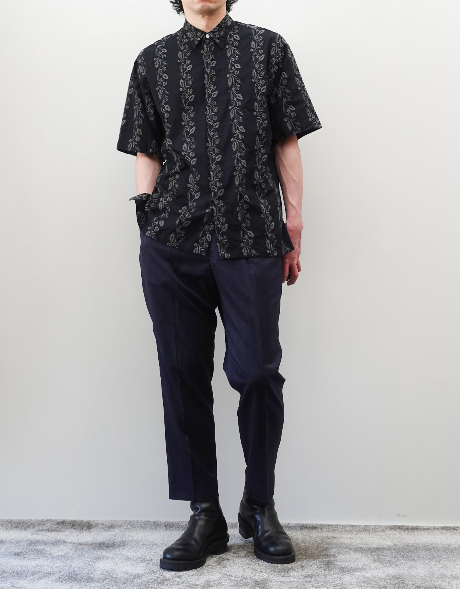 NEZU YO-HINTEN（根津洋品店）のEmbroidery Short Sleeve Shirt - Black（エンブロイダリー半袖シャツ）。前身頃に施された植物モチーフの垂直な刺繍が特徴。ブラックの生地にグレーの刺繍が映える、モードなリラックスフィットのスタイリング。モデル正面全身着用画像。