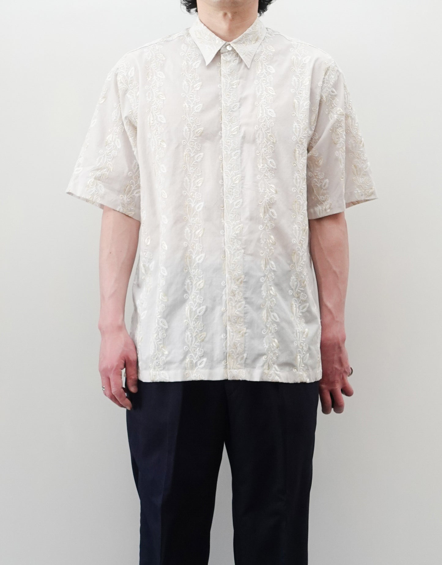NEZU YO-HINTEN（根津洋品店）のEmbroidery Short Sleeve Shirt - Off White（エンブロイダリー半袖シャツ）。前身頃に施された植物モチーフの垂直な刺繍が特徴。ブラックの生地にグレーの刺繍が映える、モードなリラックスフィットのスタイリング。モデル正面着用画像。