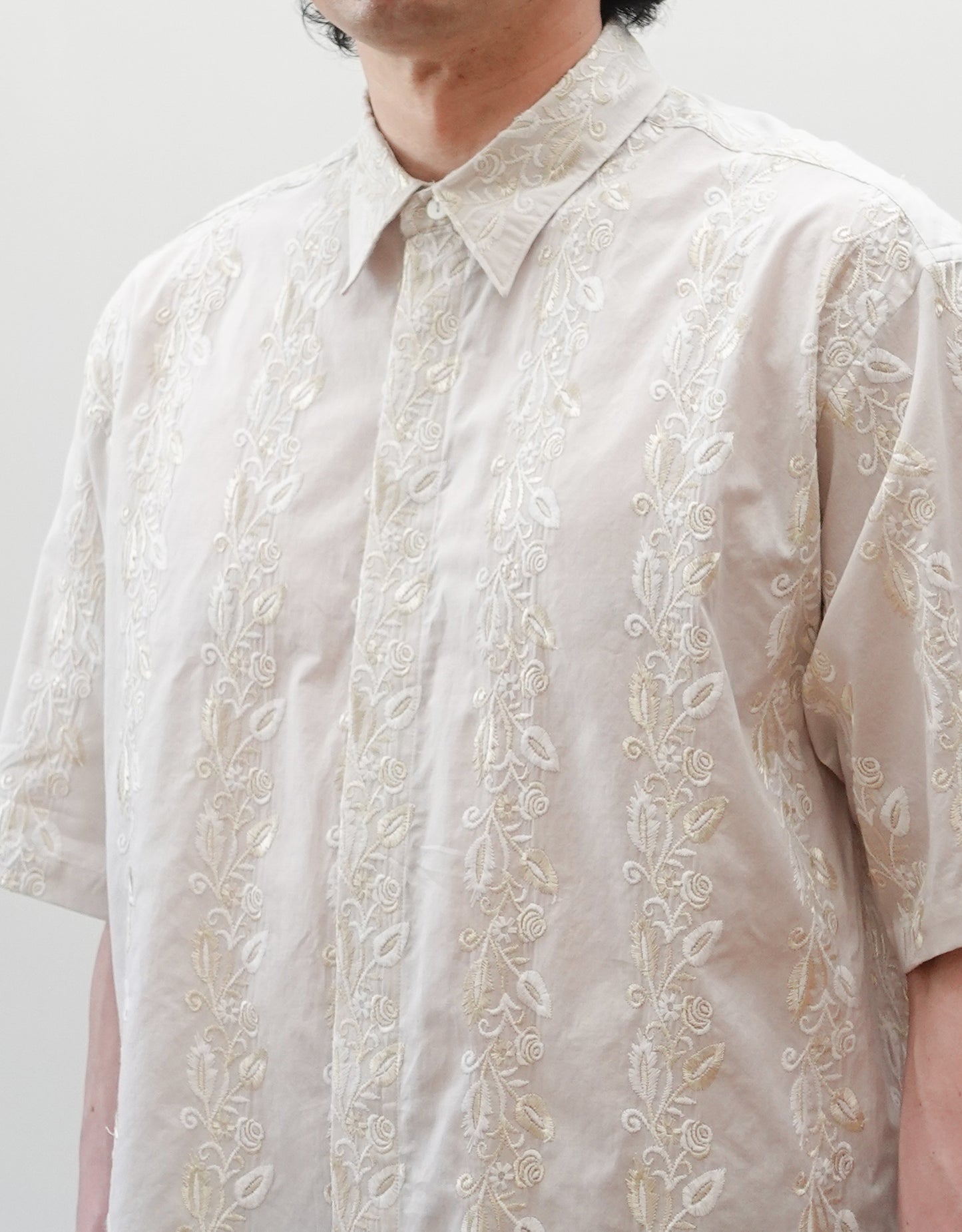 NEZU YO-HINTEN（根津洋品店）のEmbroidery Short Sleeve Shirt - Off White（エンブロイダリー半袖シャツ）。前身頃に施された植物モチーフの垂直な刺繍が特徴。ブラックの生地にグレーの刺繍が映える、モードなリラックスフィットのスタイリング。モデル着用の生地アップ画像。