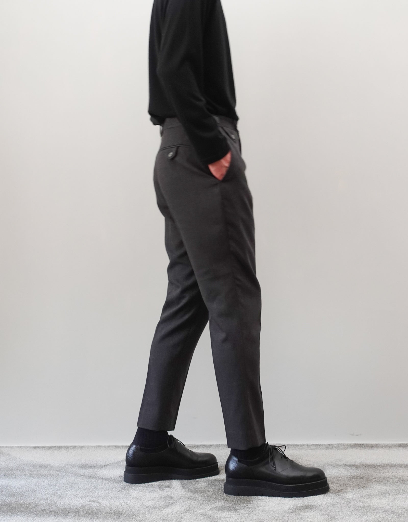 VOUILLON（ヴイヨン）のTwo Darts Slim Trousers - Gray Multi Stripe（2ダーツスリムトラウザーズ）。グレーマルチストライプ柄の端正な生地に、ウエスト回りをすっきり見せる2ダーツ仕様のスリムパンツ。美しいスリムテーパードシルエット。モデル着用左向き画像。