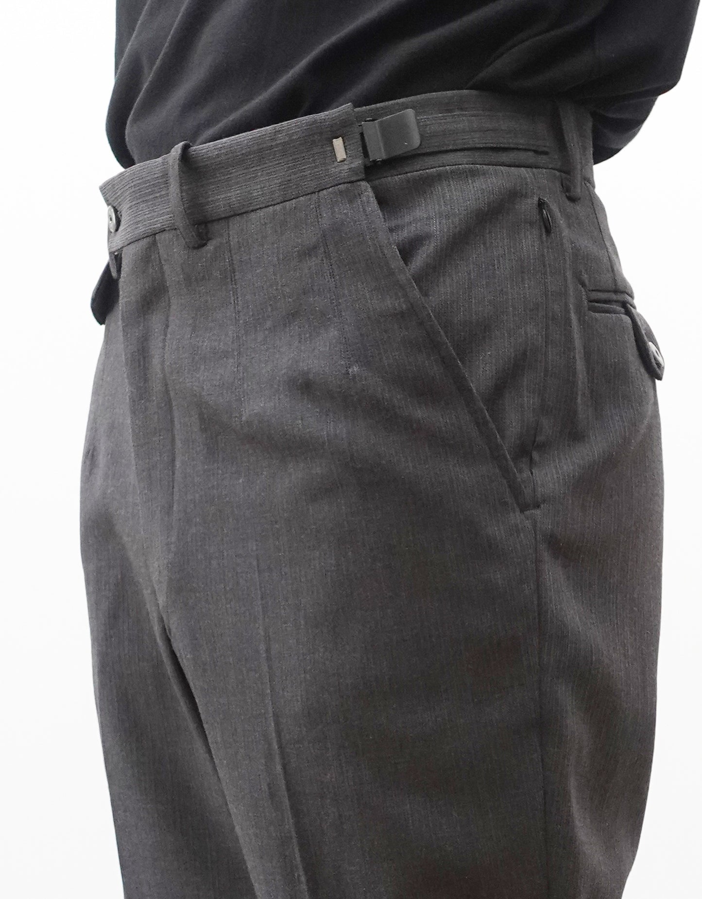 VOUILLON（ヴイヨン）のTwo Darts Slim Trousers - Gray Multi Stripe（2ダーツスリムトラウザーズ）。グレーマルチストライプ柄の端正な生地に、ウエスト回りをすっきり見せる2ダーツ仕様のスリムパンツ。美しいスリムテーパードシルエット。モデル着用ウエスト左でアジャスターベルト最大開き見本画像。
