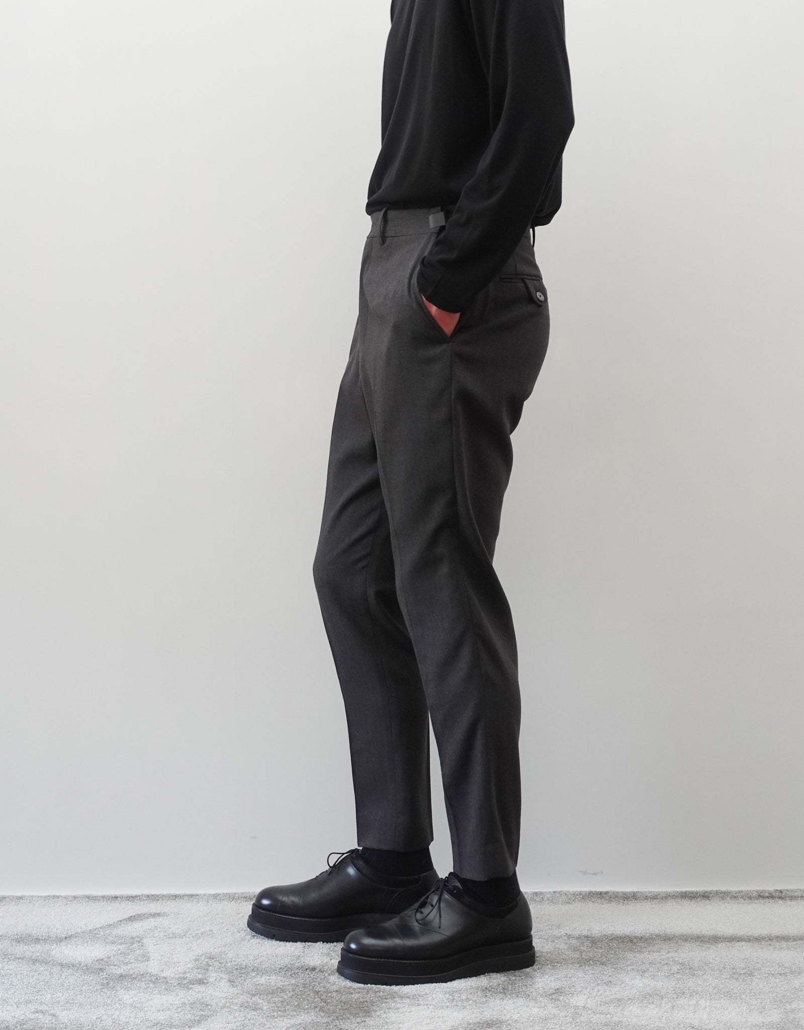 VOUILLON（ヴイヨン）のTwo Darts Slim Trousers - Gray Multi Stripe（2ダーツスリムトラウザーズ）。グレーマルチストライプ柄の端正な生地に、ウエスト回りをすっきり見せる2ダーツ仕様のスリムパンツ。美しいスリムテーパードシルエット。モデル着用右向き画像。