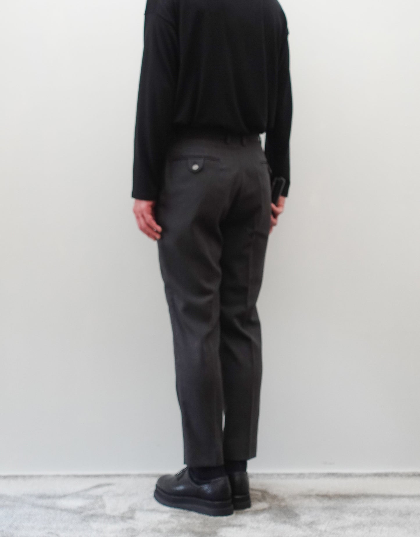 VOUILLON（ヴイヨン）のTwo Darts Slim Trousers - Gray Multi Stripe（2ダーツスリムトラウザーズ）。グレーマルチストライプ柄の端正な生地に、ウエスト回りをすっきり見せる2ダーツ仕様のスリムパンツ。美しいスリムテーパードシルエット。モデル着用背面画像。