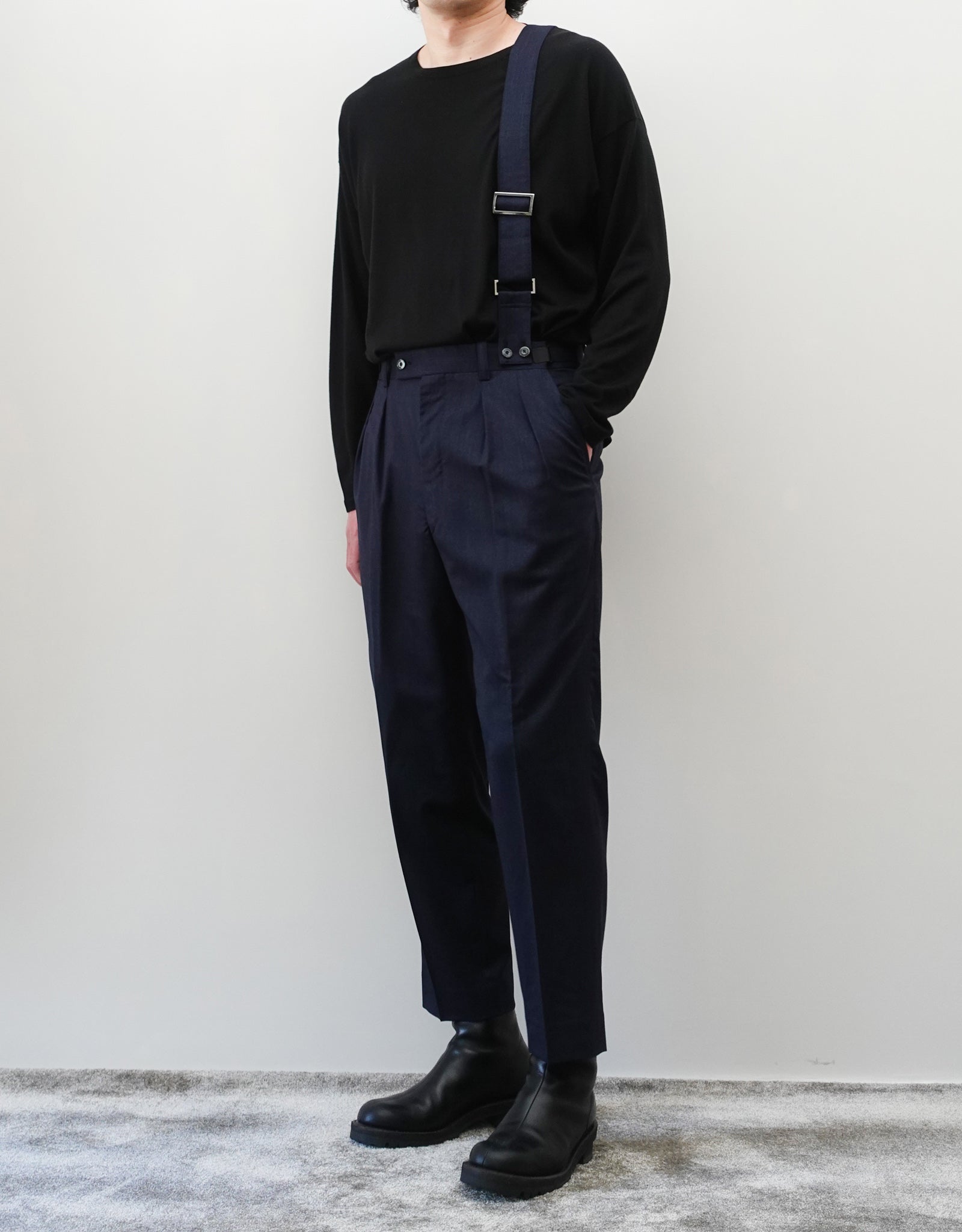 VOUILLON（ヴイヨン）のSuspender Two Tuck Trousers - Navy（サスペンダーツータックトラウザーズ）。ネイビーのツータックワイドパンツに、取り外し可能な同素材のサスペンダーを備えたディテール。モデル着用正面画像。