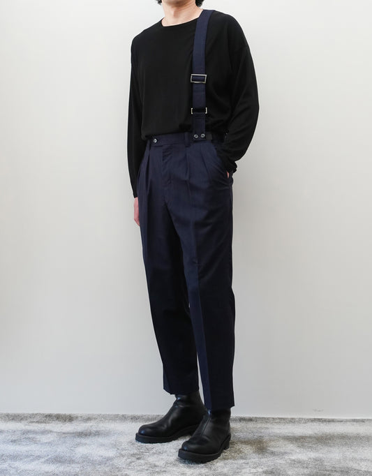 VOUILLON（ヴイヨン）のSuspender Two Tuck Trousers - Navy（サスペンダーツータックトラウザーズ）。ネイビーのツータックワイドパンツに、取り外し可能な同素材のサスペンダーを備えたディテール。モデル着用正面画像。
