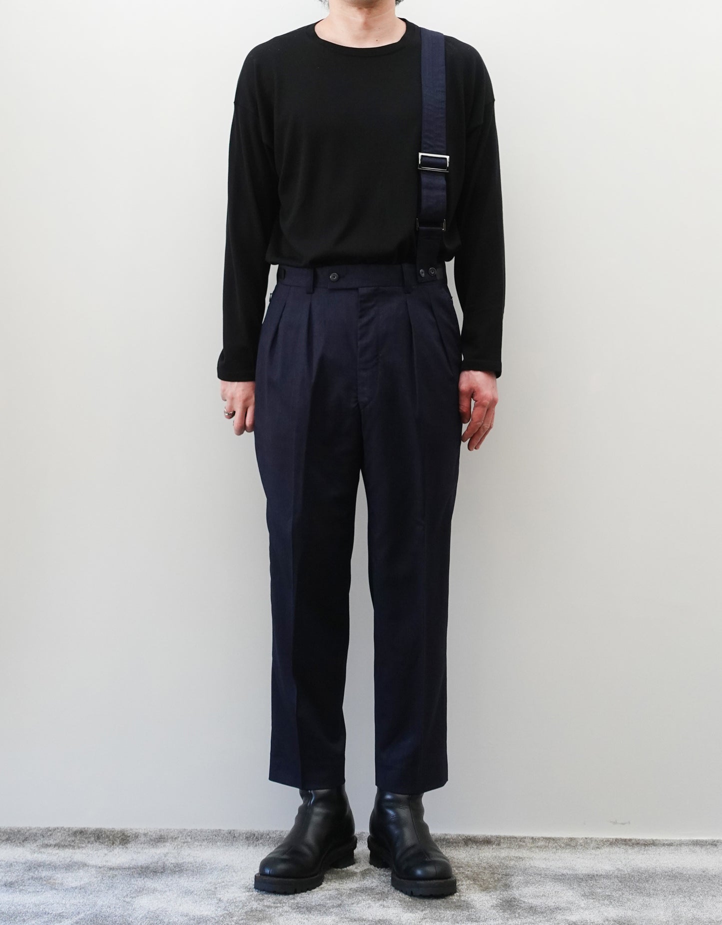 VOUILLON（ヴイヨン）のSuspender Two Tuck Trousers - Navy（サスペンダーツータックトラウザーズ）。ネイビーのツータックワイドパンツに、取り外し可能な同素材のサスペンダーを備えたディテール。モデル着用正面全身画像。