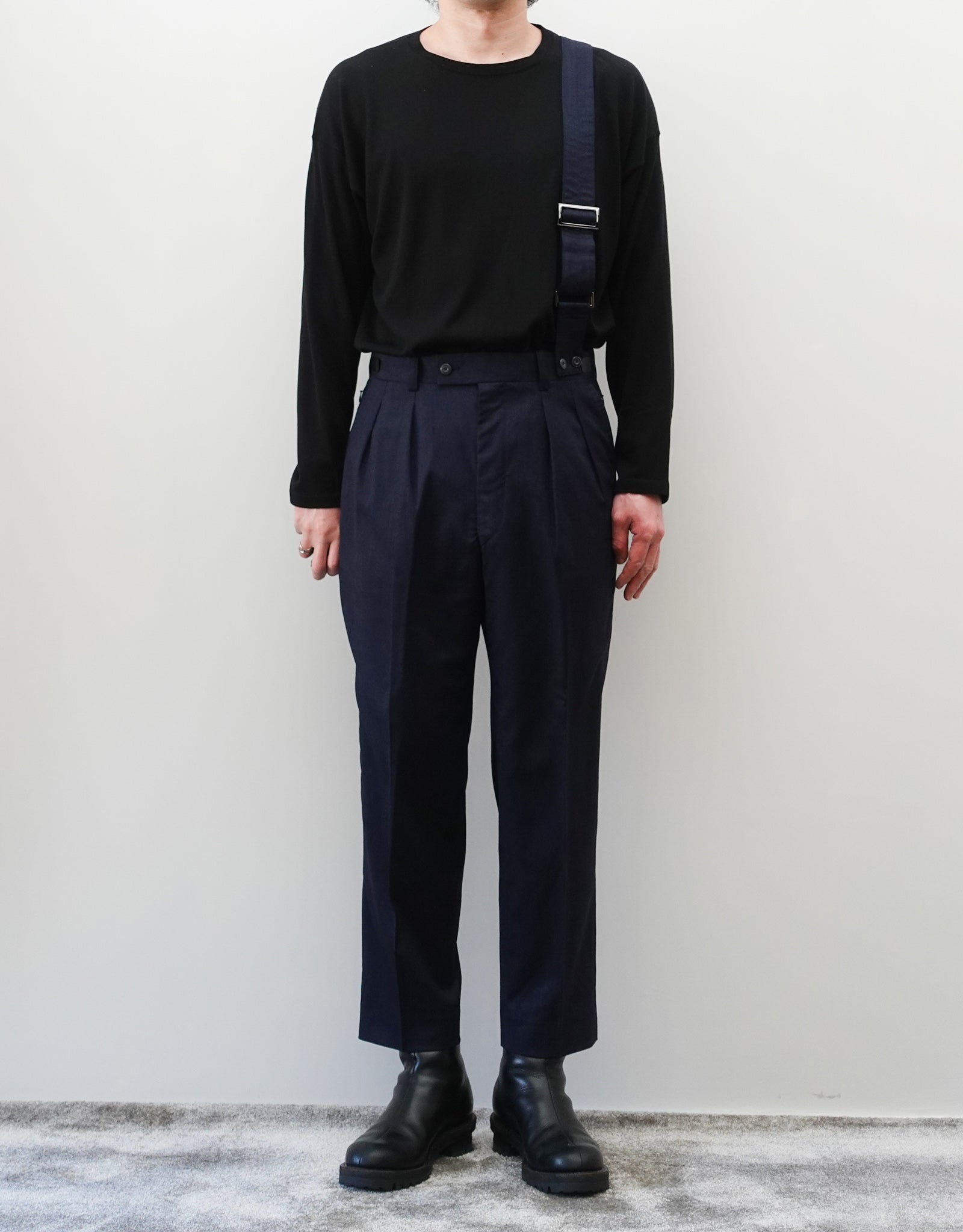 VOUILLON（ヴイヨン）のSuspender Two Tuck Trousers - Navy（サスペンダーツータックトラウザーズ）。ネイビーのツータックワイドパンツに、取り外し可能な同素材のサスペンダーを備えたディテール。モデル着用正面全身画像。